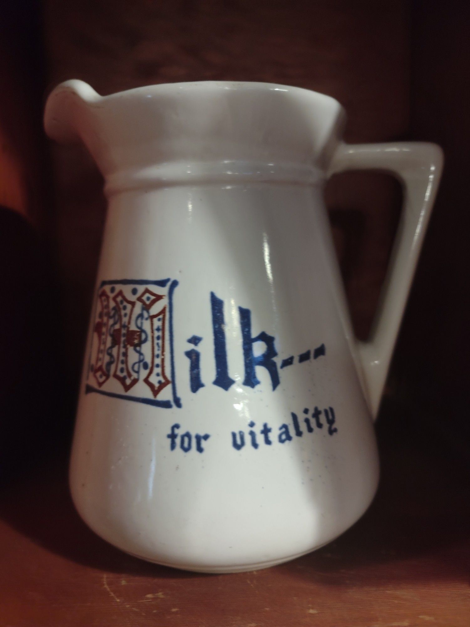 A picture of a ceramic white pitcher. It has blue text on it that says "Milk... for vitality"