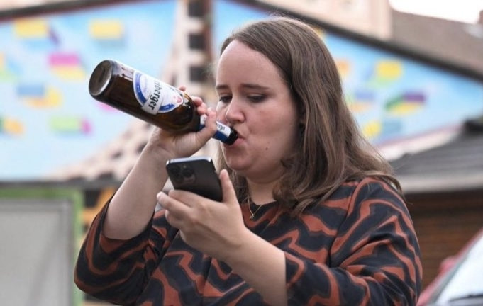 Foto von Ricarda Lang wie sie Bier trinkend auf ihr Handy schaut.