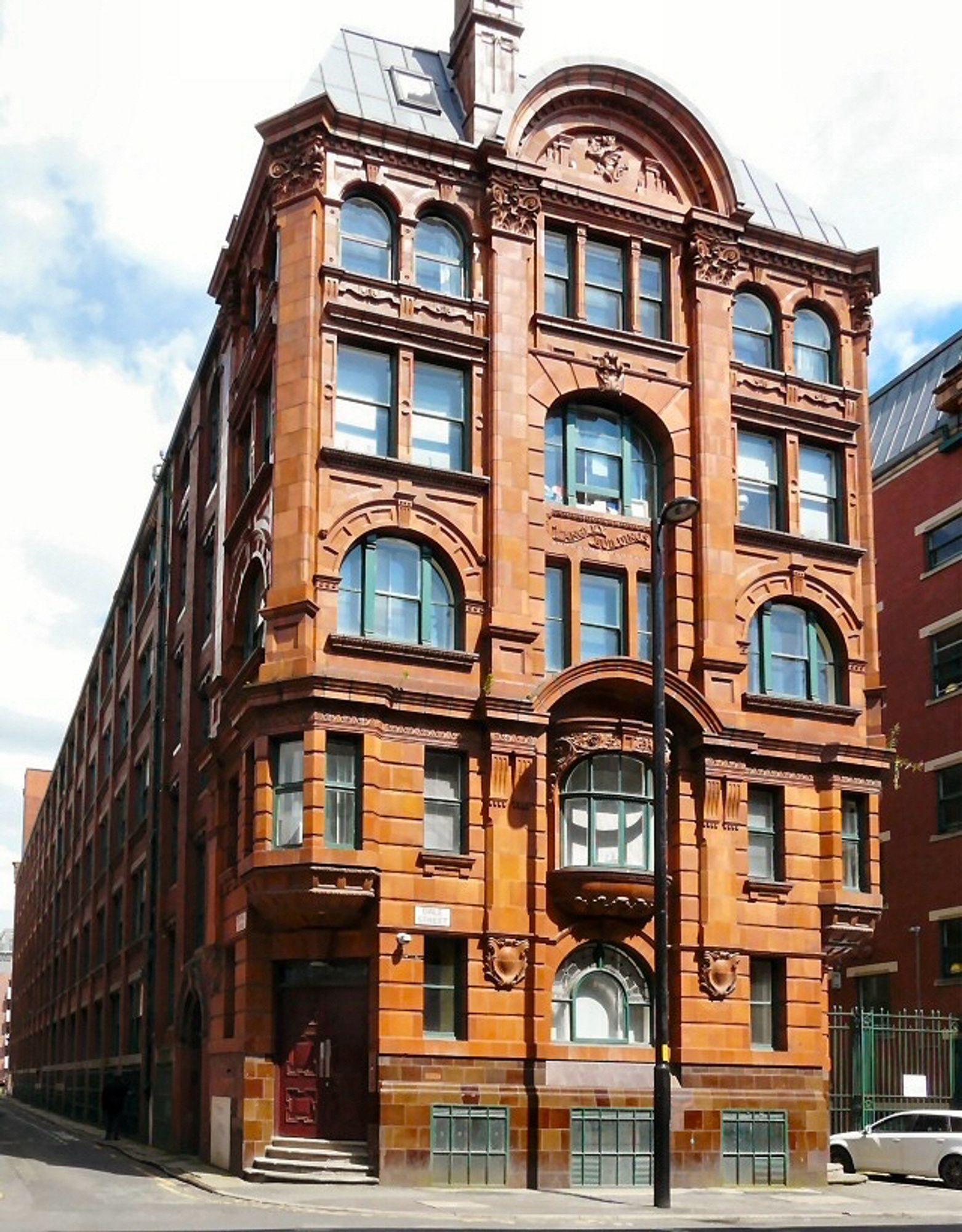 Front view of large ornate Victorian warehouse, with a tiled lower exterior, many windows of different styles, brickwork also ornate with much detailing, warm brown/orange in colour. 
©️Gerald England Creative Commons licence