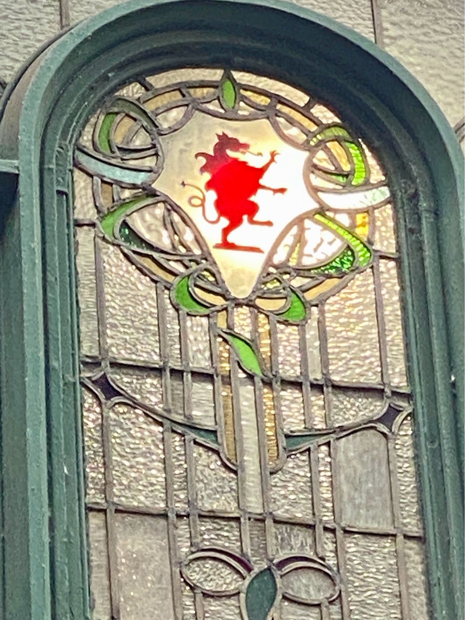 Victorian stained glass leaded window in art nouveau style, at the top there is a red dragon balancing on one foot with paws outstretched.