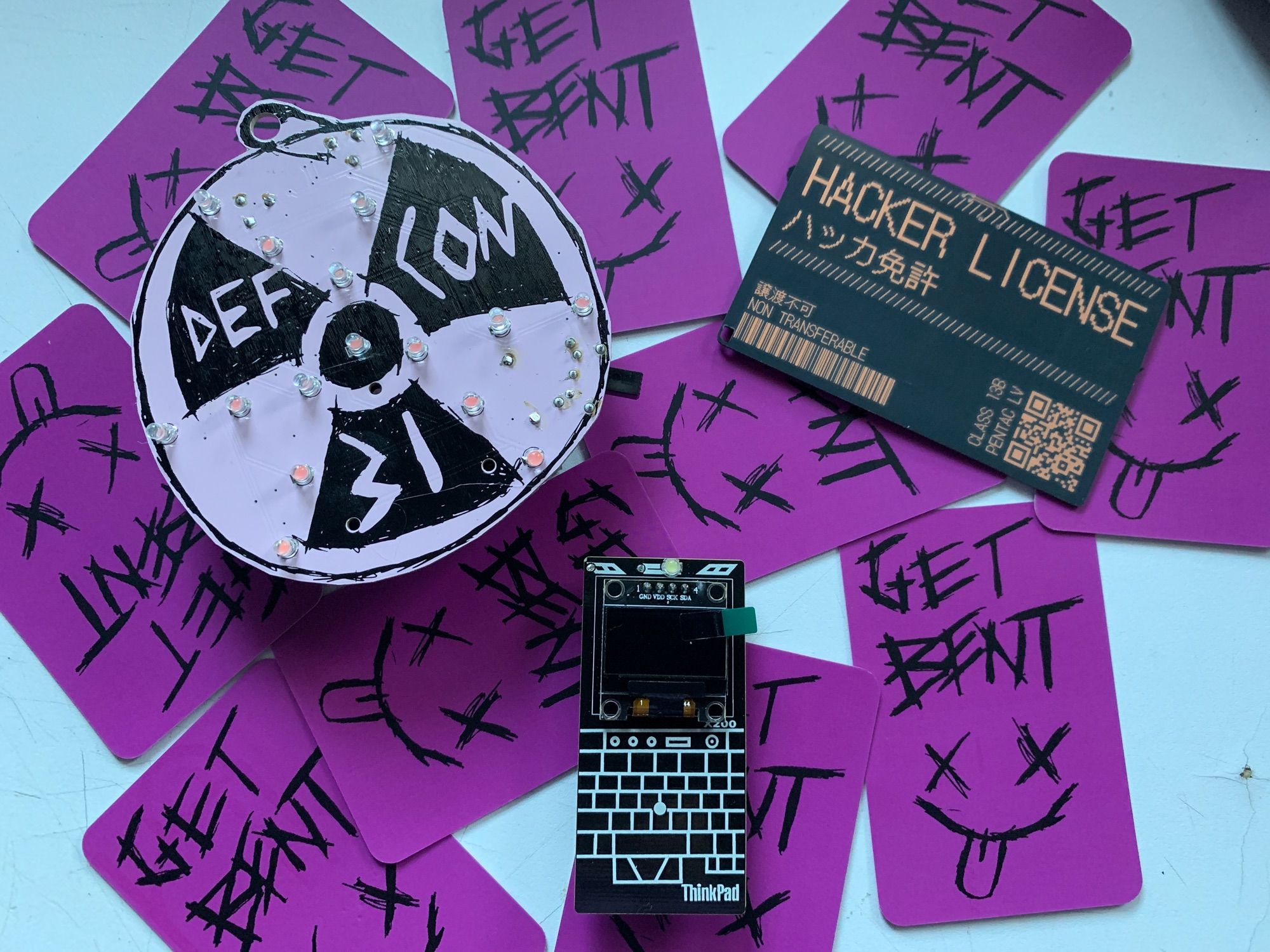 3 PCB badges on a background of purple business cards that say Get Bent