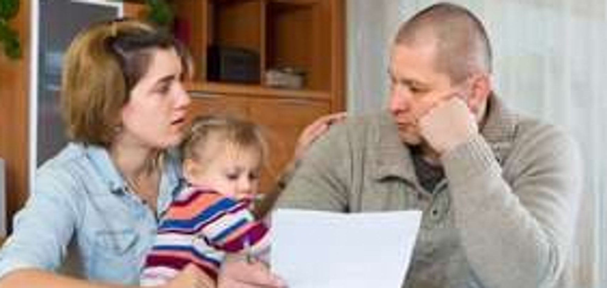 Stock photo d'un couple en train de regarder une feuille de paye avec leur bébé sur les genoux.