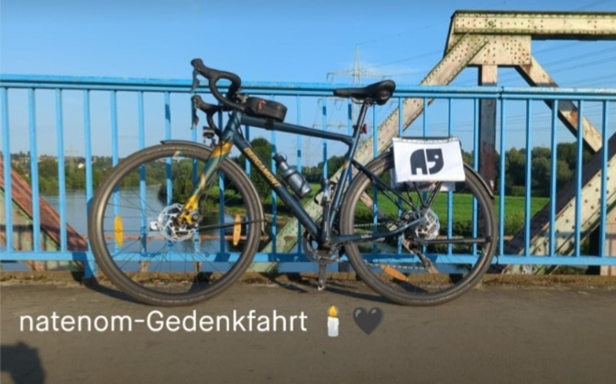 Foto: Ein Gravelbike lehnt vor blauem Himmel an einem Brückengeländer. Am Gepäckträger ist ein Ausdruck eines schwarzen, stilisierten Elefanten auf weißem Hintergrund befestigt.