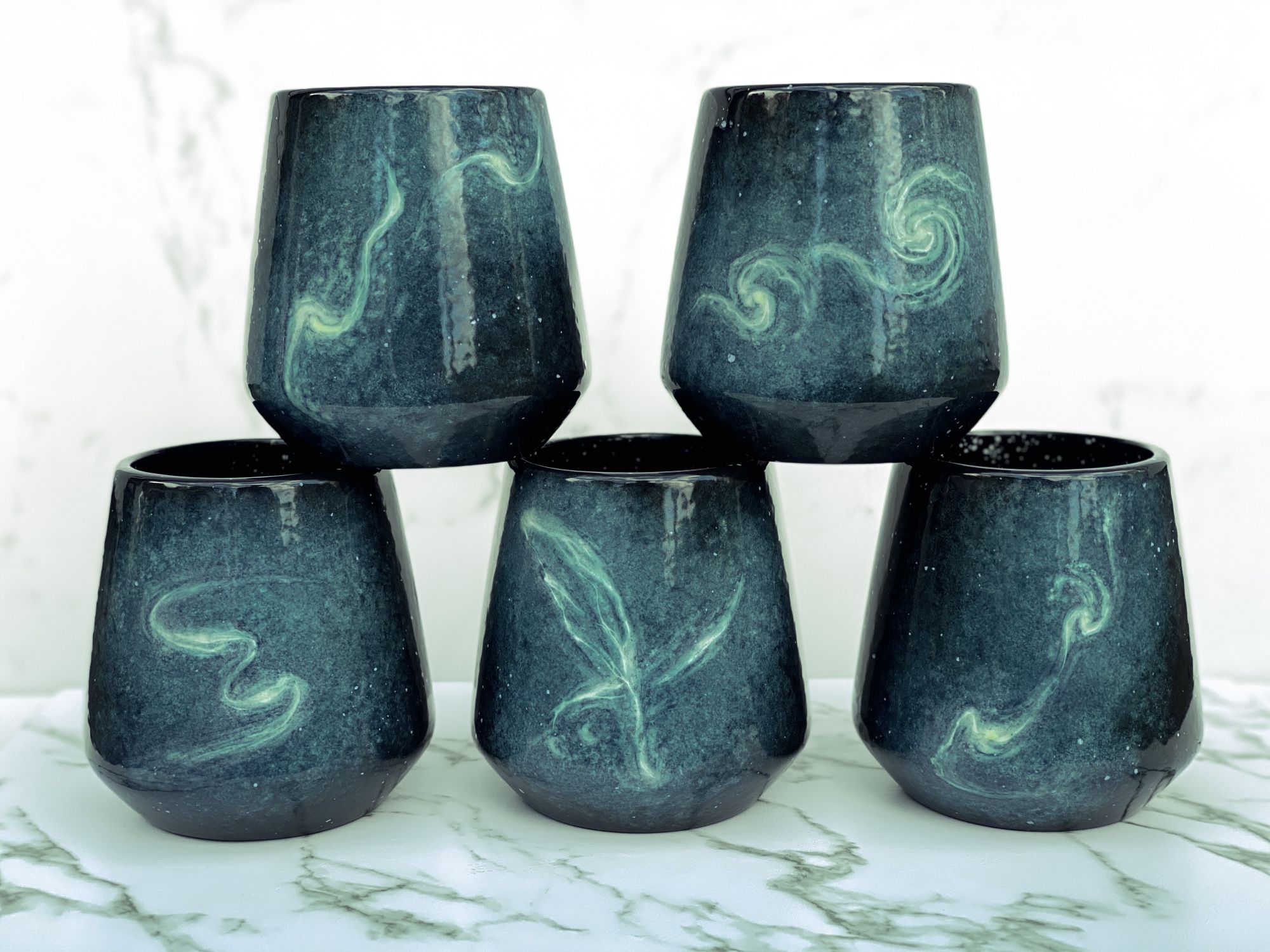 Five angled cups featuring painterly renditions of interacting galaxies in shades of blue and teal.