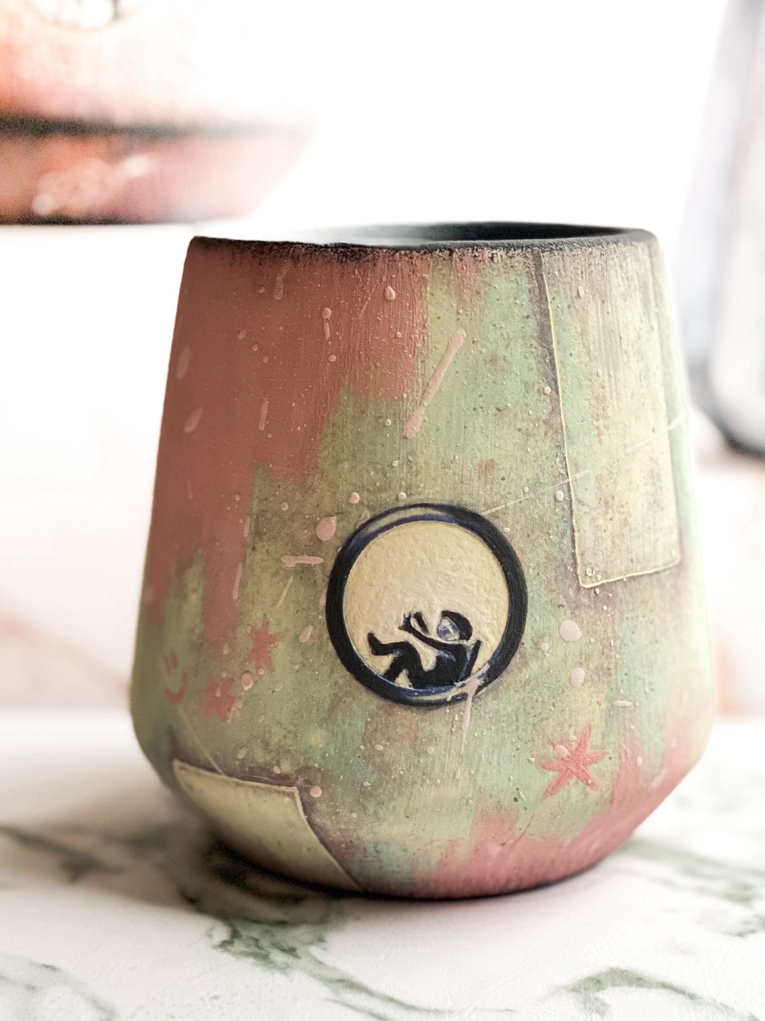 Center cup featuring a pale green rusty exterior partially painted in pink while an astronaut seen through a round window reclines and paints their nails.