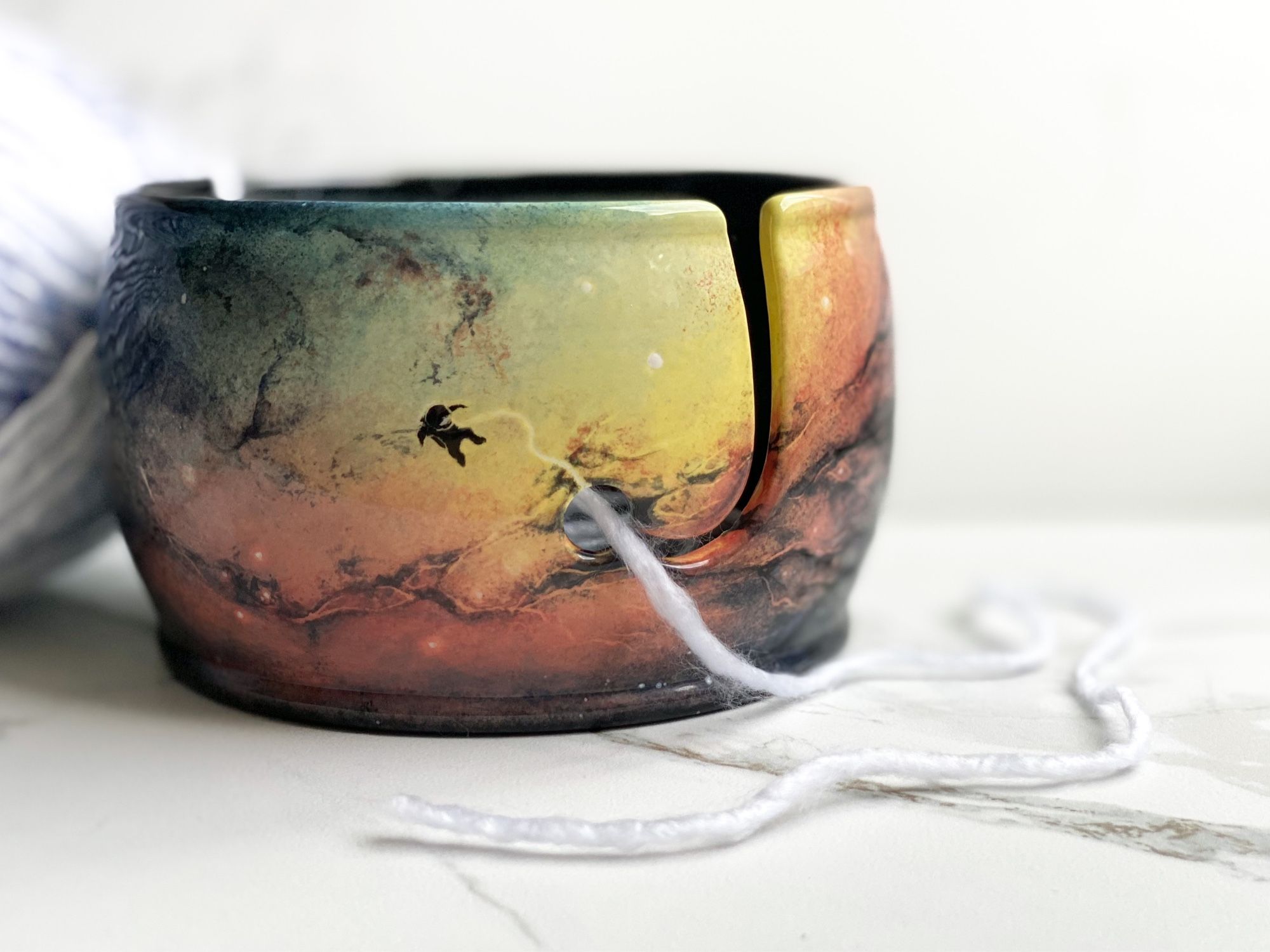 Yarn bowl featuring colorful nebula with floating astronaut attached to a tether that leads to the yarn feed.