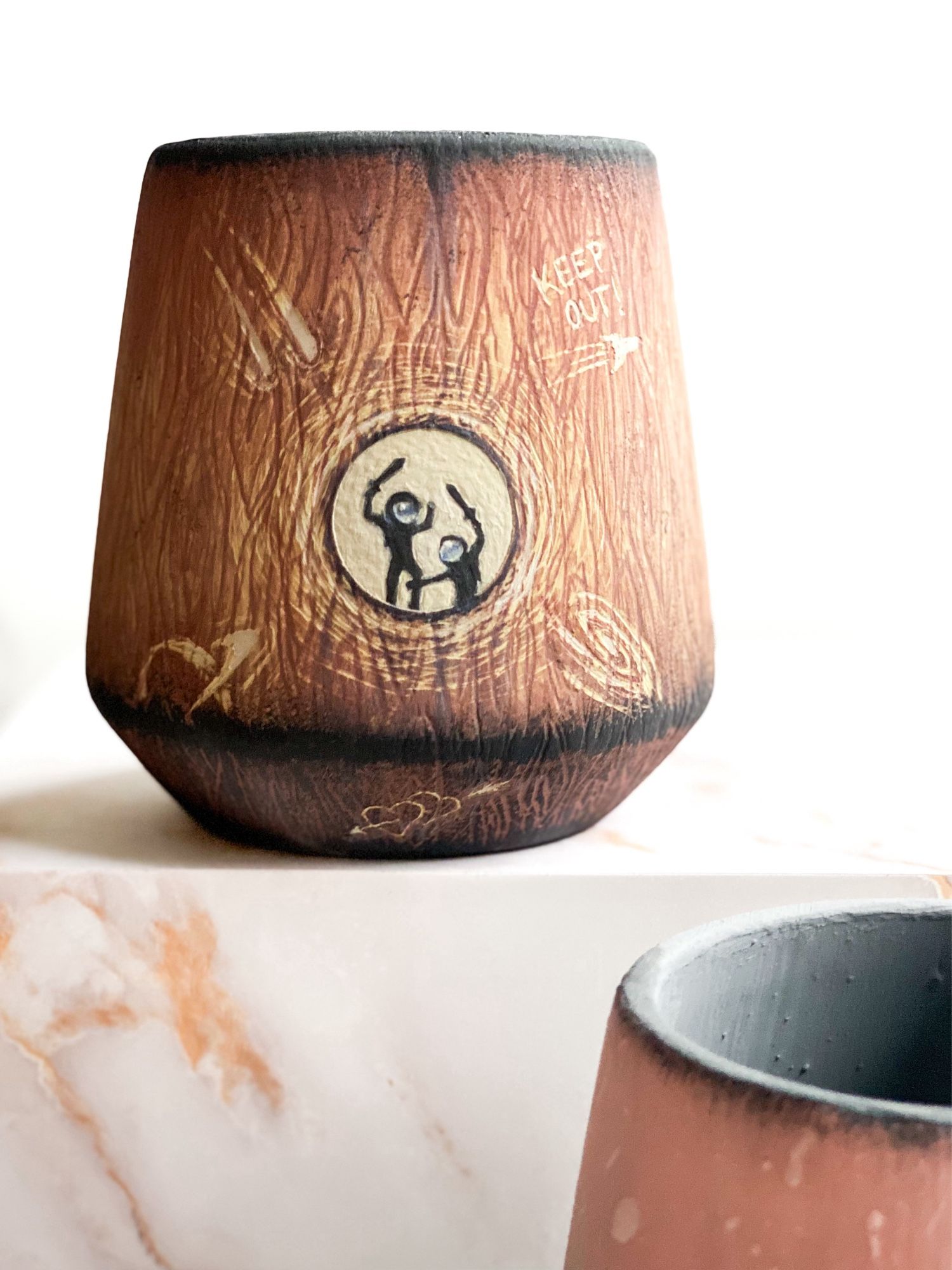 Left cup featuring a woodgrain pattern with childlike carvings and two astronauts seen through a round window playing with swords