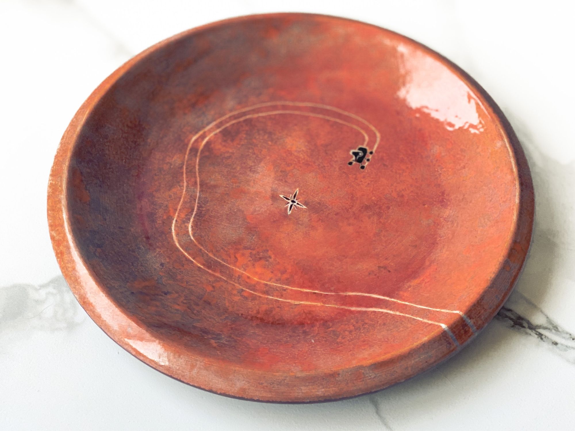 Plate painted like a Mars crater with Perseverance rover making tracks in a circular direction and Ingenuity helicopter flying above.