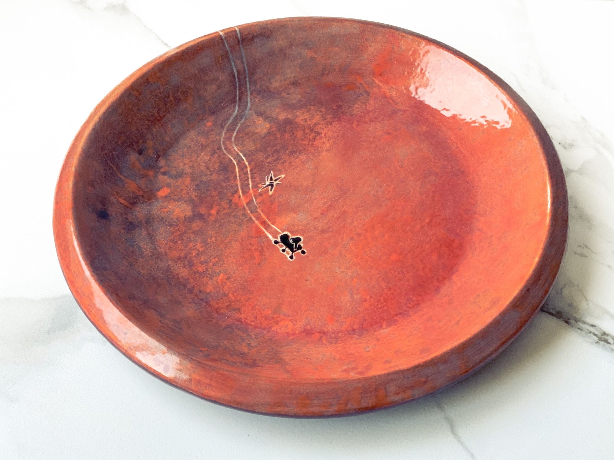 Plate painted like a Mars crater with Perseverance rover making tracks down the center and Ingenuity helicopter flying above (side view)