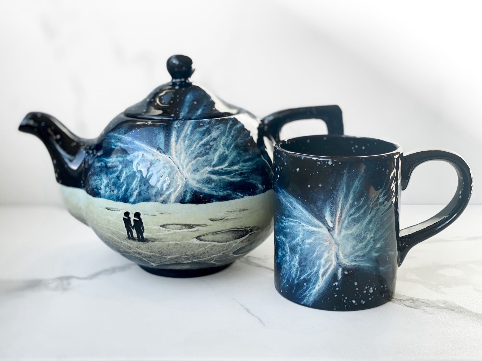 Teapot and mug with the Butterfly Nebula. Teapot also has a cratered landscape below with two astronauts holding hands looking toward the horizon.