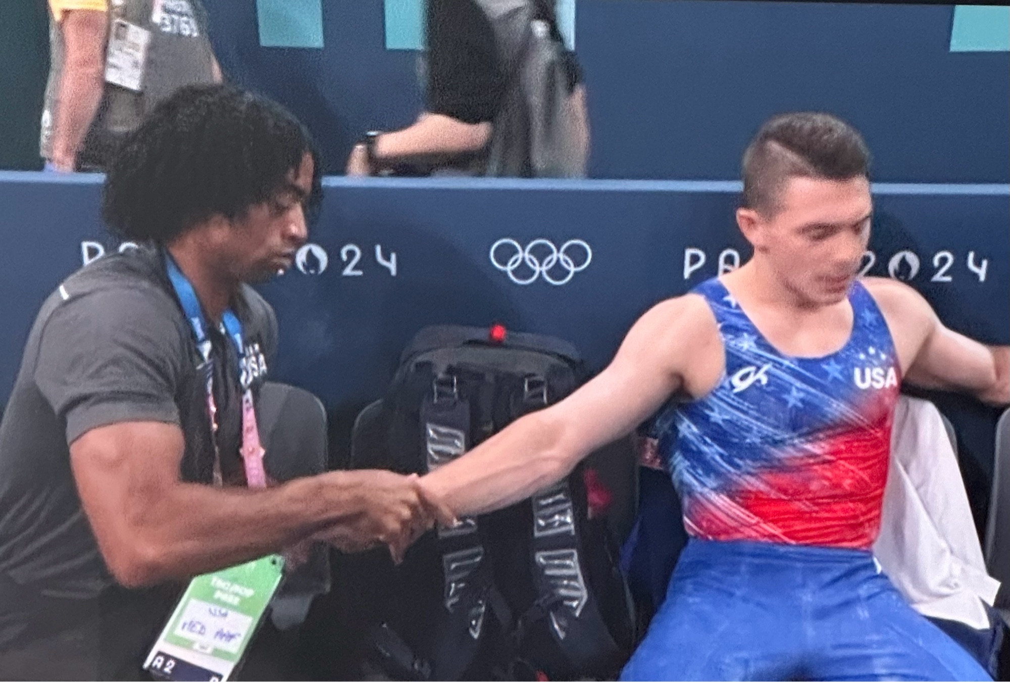 an athletic trainer massages the forearm of a gymnast between events during the all-around men’s gymnastics final