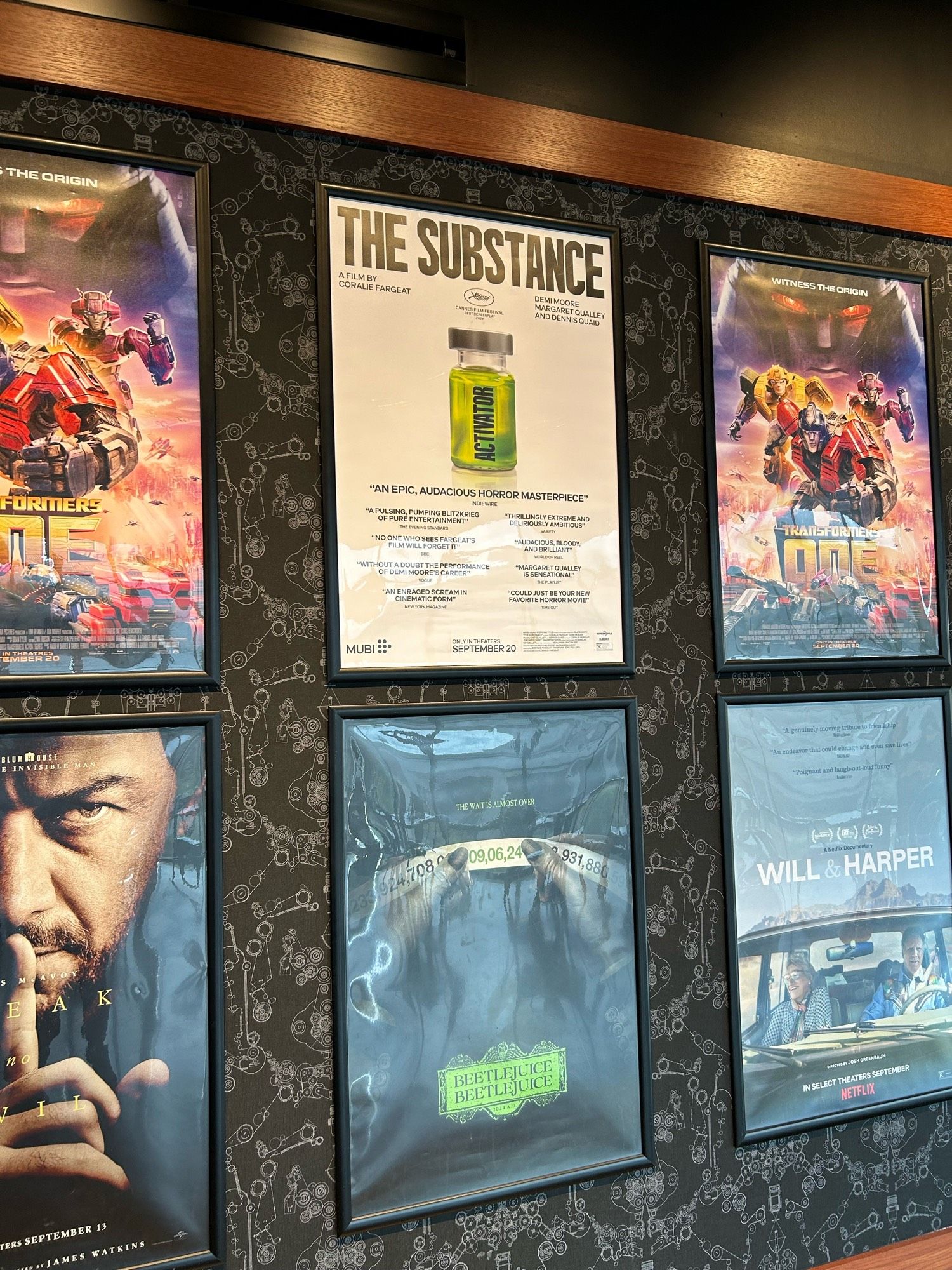 Posters for The Substance and Beetlejuice Beetlejuice in the Alamo Drafthouse lobby. The Beetlejuice poster is obscured by the light coming in through the outside windows.