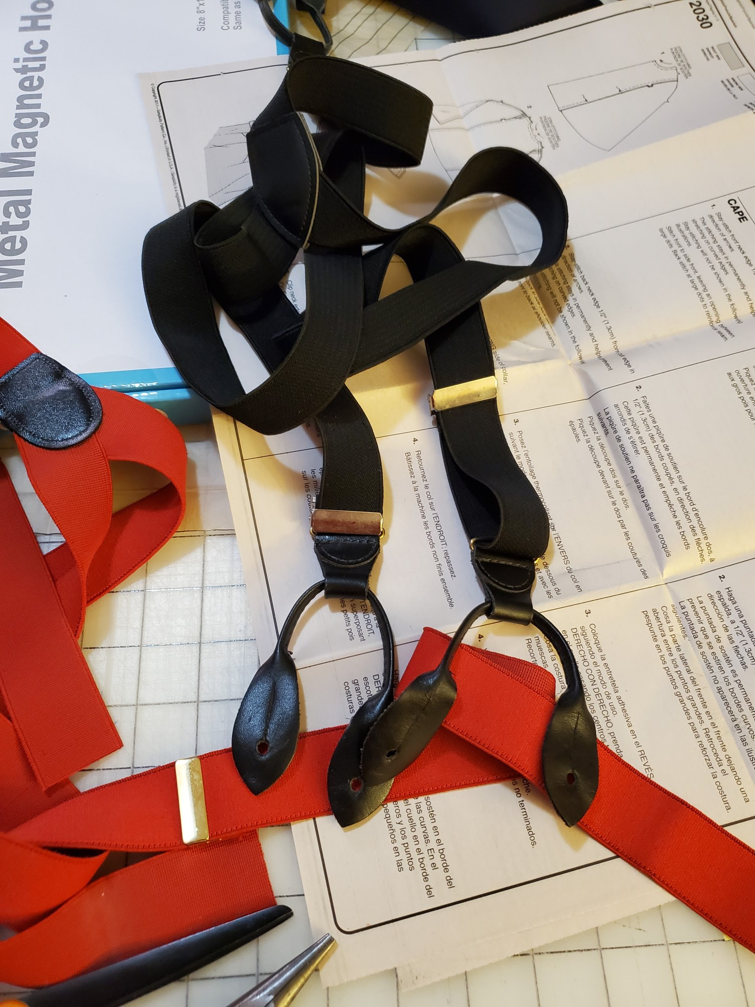 A set of red and a set of black suspenders on a messy work table.