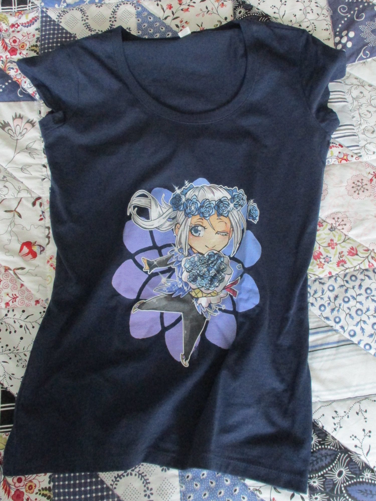 A dark-blue T-shirt with a chibi art of Viktor on the front He's winking and wearing the blue-scale costume he wore when he and Chris first met. On his head is a crown made of blue roses and he's holding a bouquet with blue flowers in one hand. The background is a blue-and-purple flower pattern.