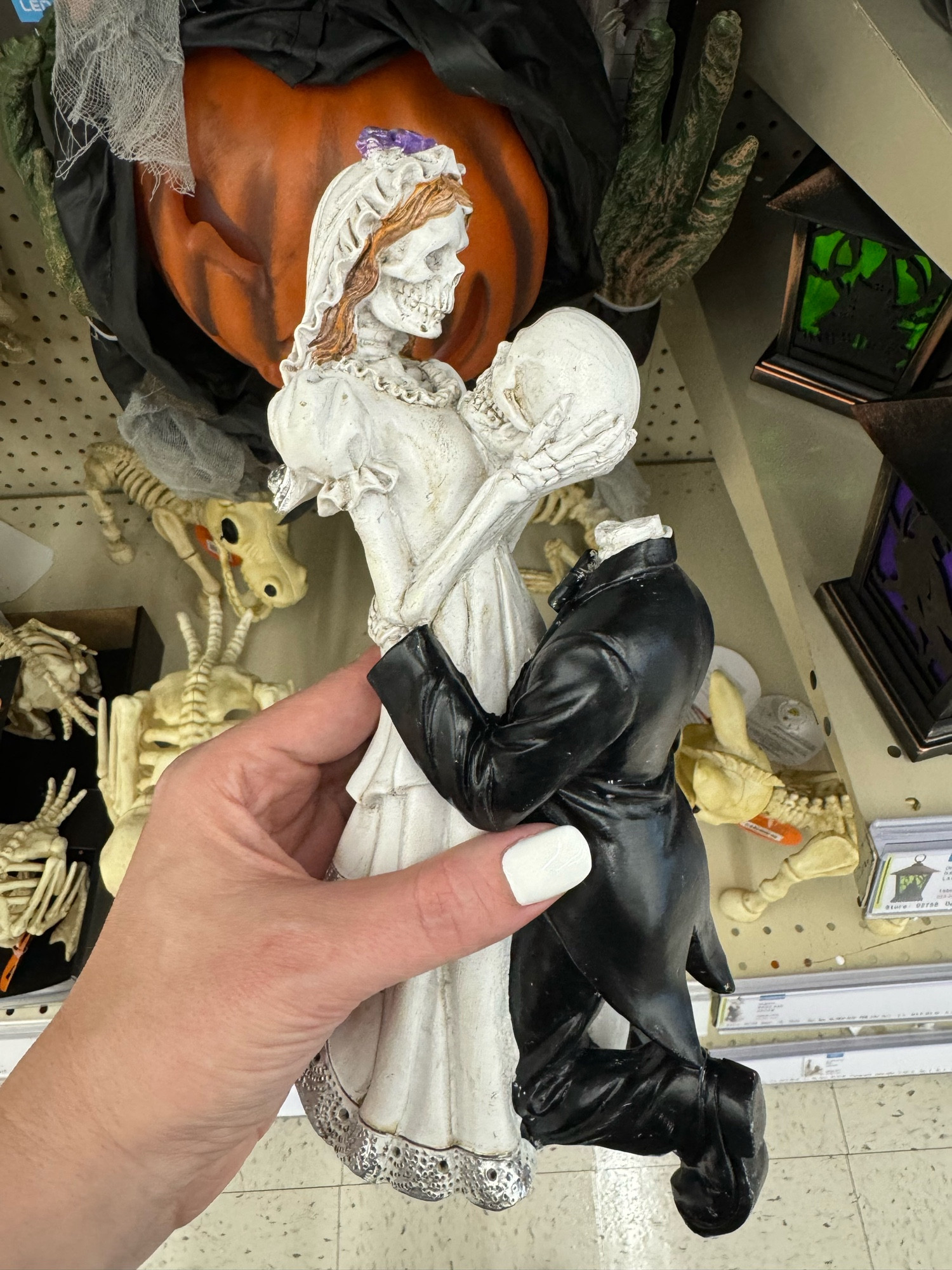 halloween decor statue of a skeleton bride and groom: the groom is on one knee and holding the bride’s waist, and the bride has his detached skull in her hands