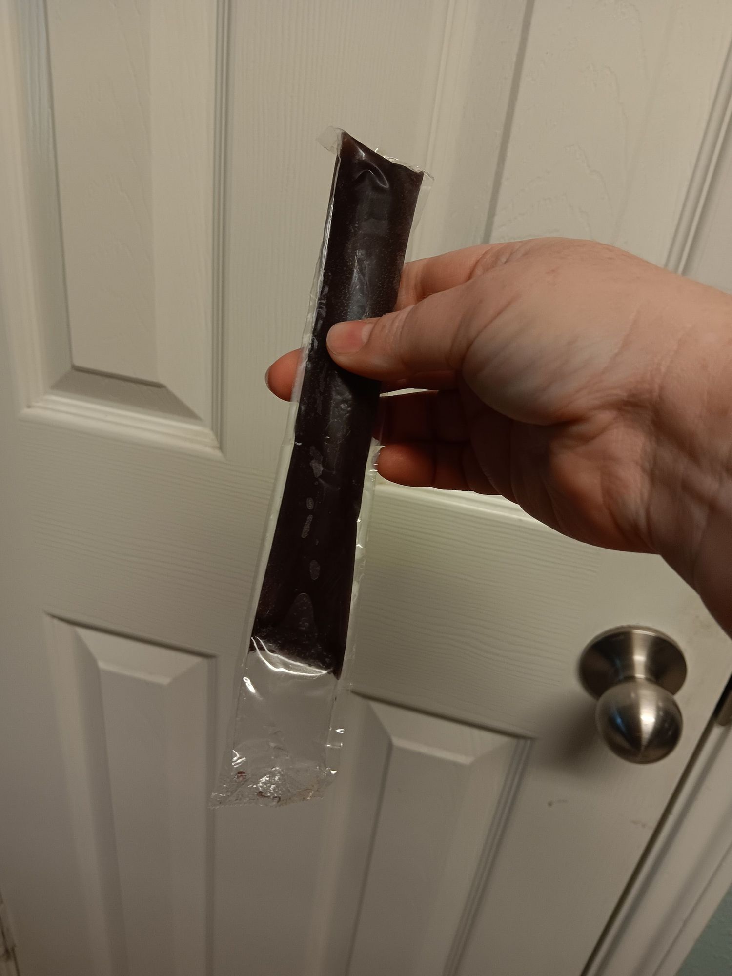 Holding a grape-flavored freeze pop so that there is an inch of empty plastic at the bottom.