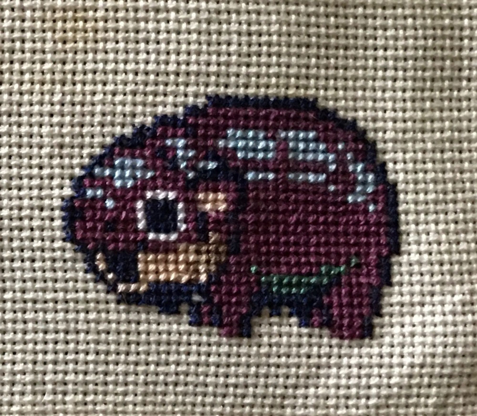 Pixelated version of Moo Deng, Pygmy Hippopotamus in Thailand zoo, mouth open in a scream, rendered into cross stitch on aida fabric.