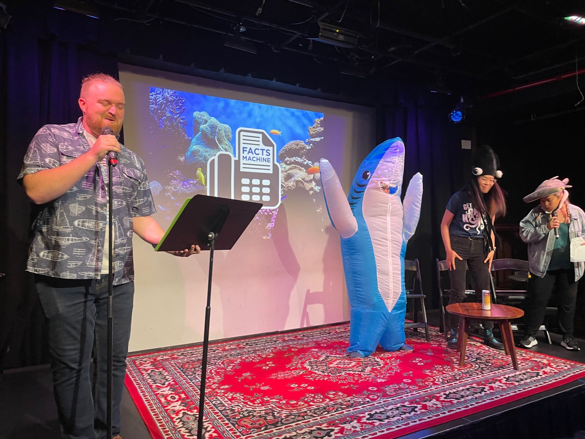 Jaida in a giant inflatable shark costume on stage for the Facts Machine live podcast at Caveat in NYC.