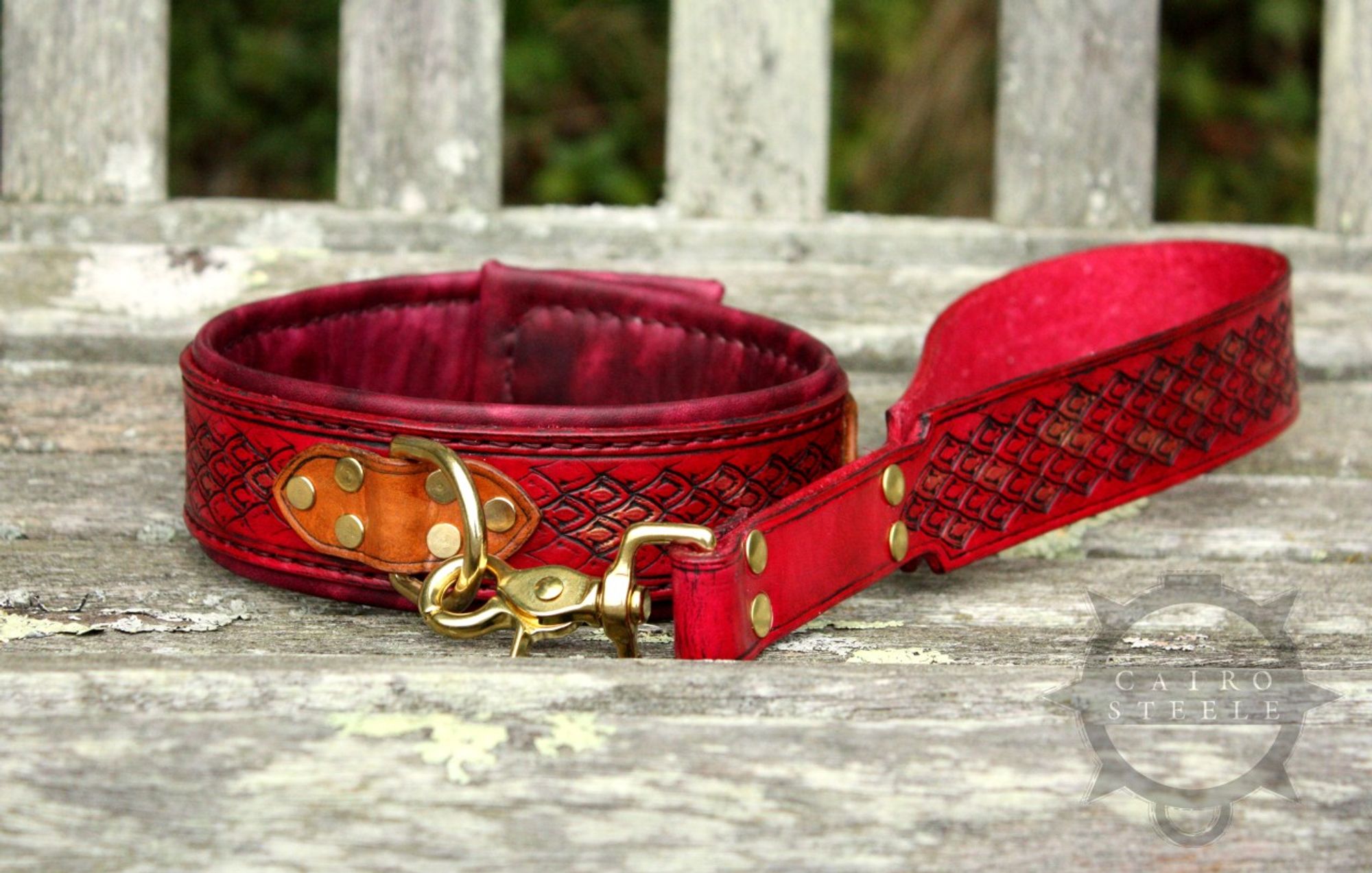 A handmade leather collar with a matching short leash. It has a vibrant red base strap with dragonscale tooling, with accent scales picked out in metallic gold and copper. The top straps are golden brown, the liner is burgundy, and the hardware is brass.