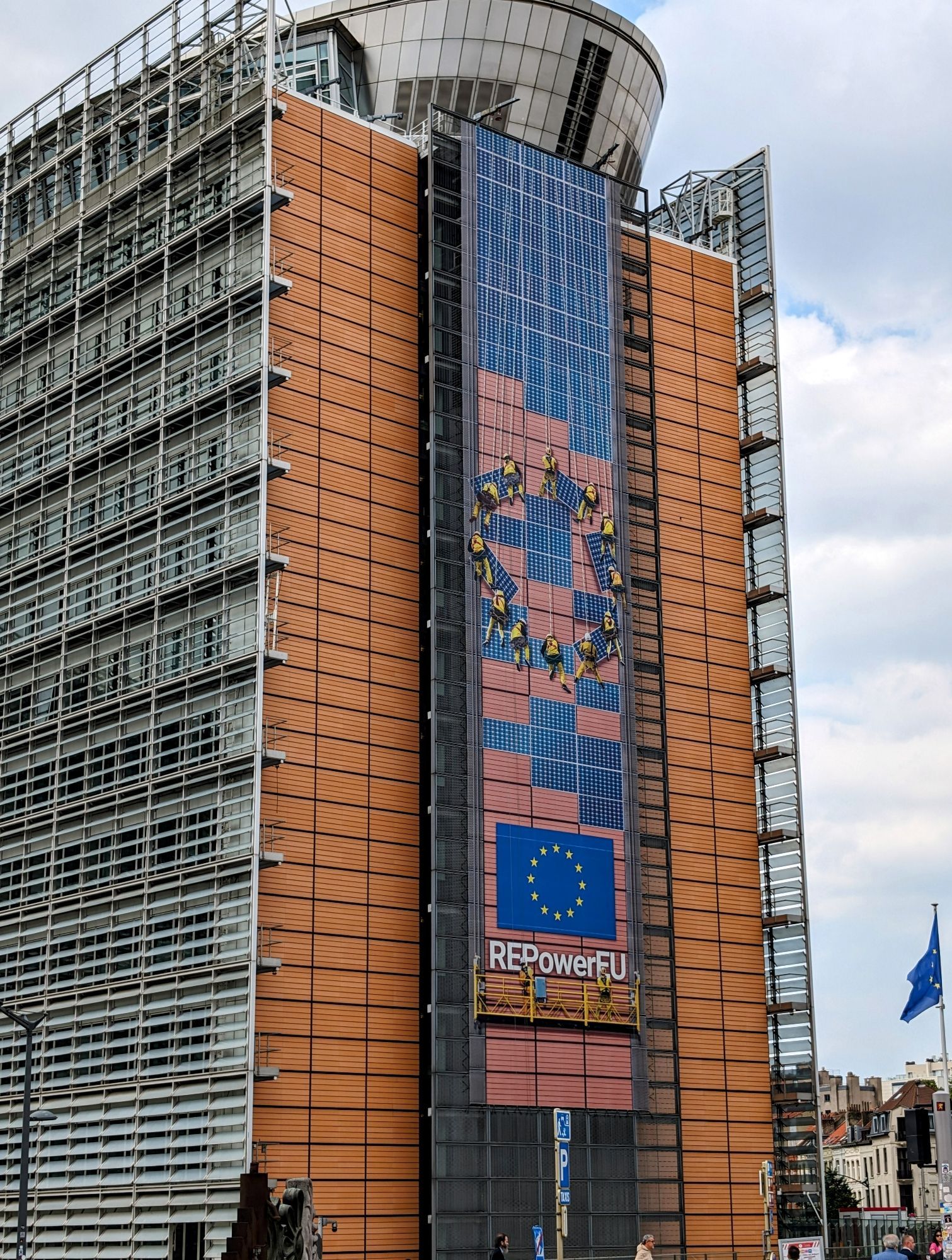 Kommissionsgebäude in Brüssel mit der Aufschrift REPowerEU. Großes Plakat, 12 im Kreis angeordnete Arbeiter im gelben Gewand montiere PV Platten.