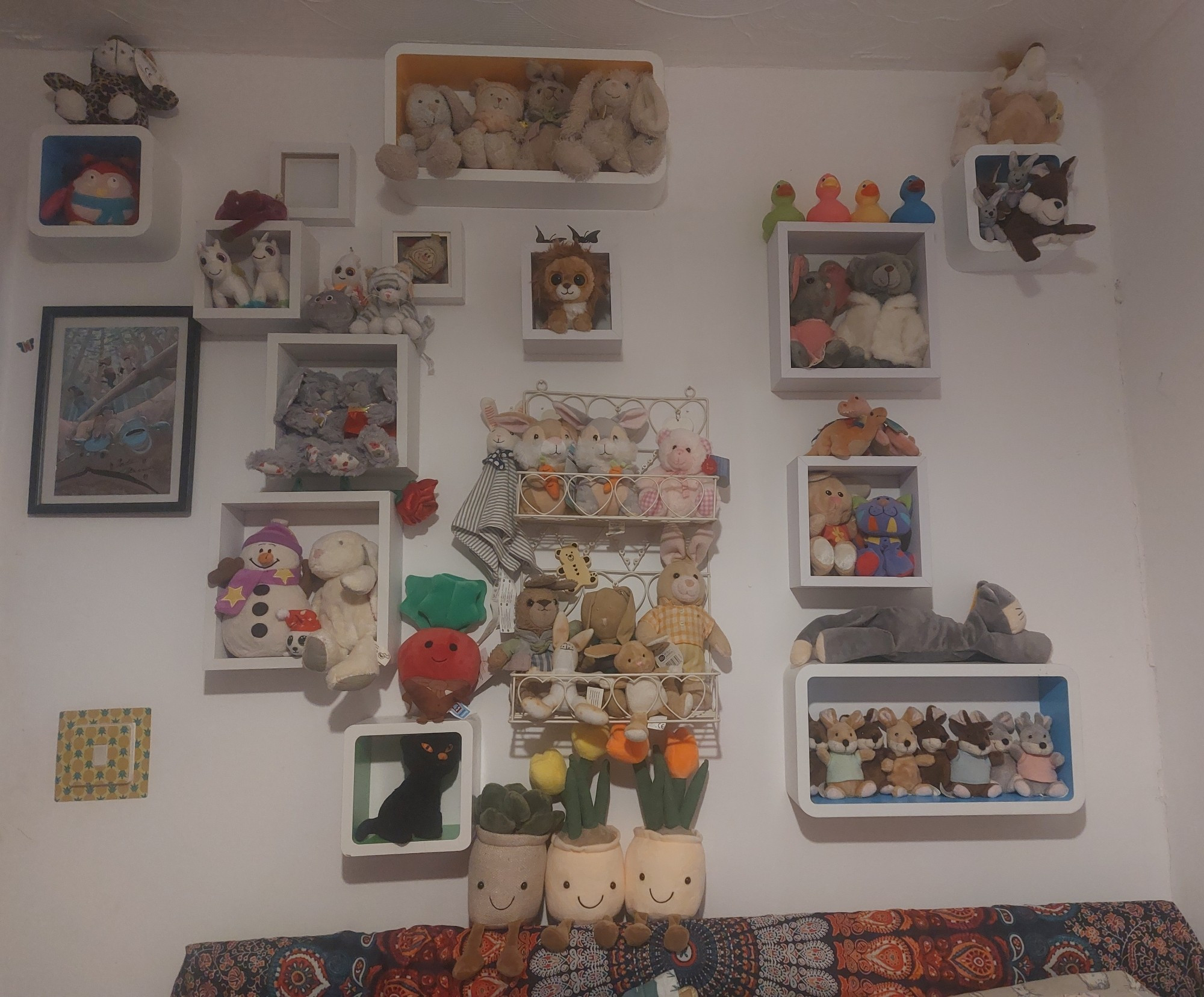 The wall over my bed, covered in a selection of white shelves filled with mostly soft toys, but also rubber ducks and a couple of antique metal butterflies.