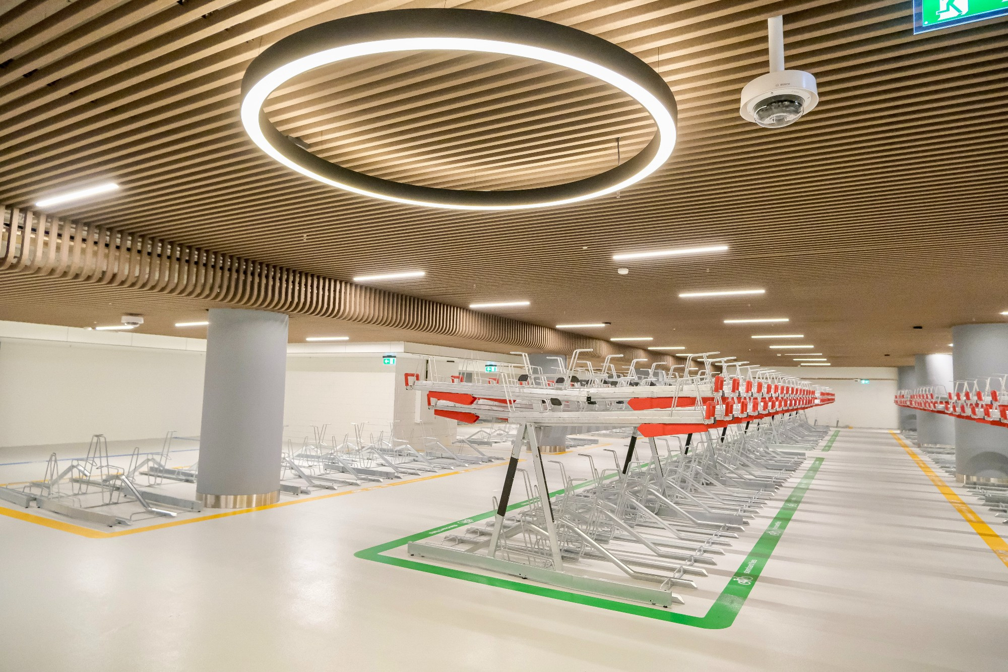 An underground bike parking facility in the city center of Rotterdam contains two-tiered metal racks, decorative lighting fixtures, and wood panelling on the ceiling.