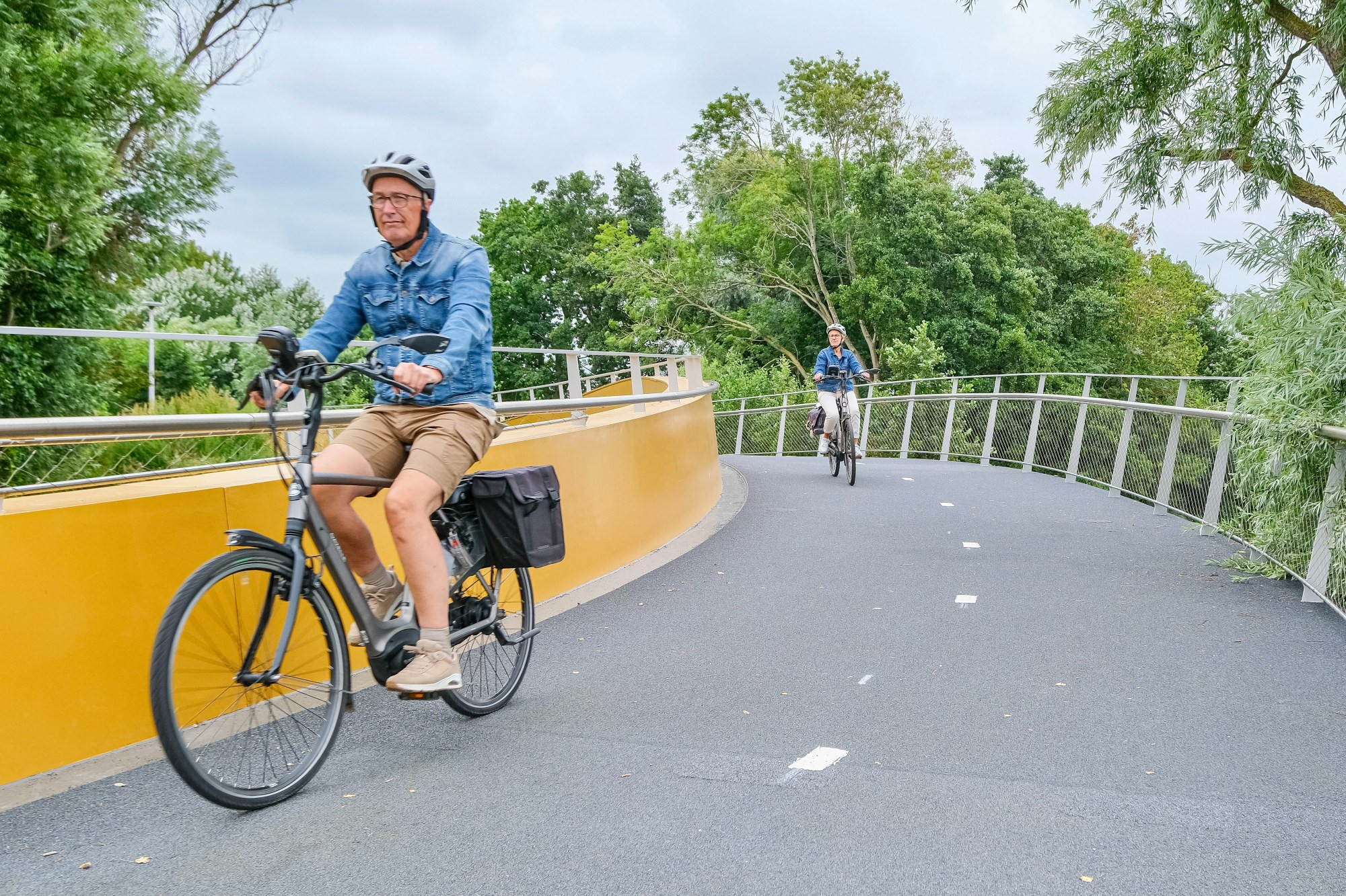 Photographs of a yellow and grey curved steel cycling bridge that stretches across a canal in Voorhout in the rural Netherlands.