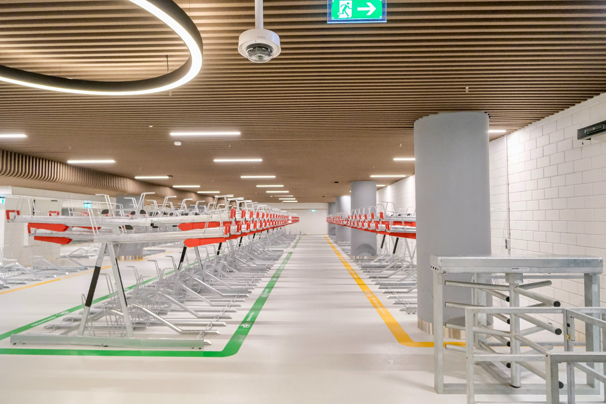 An underground bike parking facility in the city center of Rotterdam contains two-tiered metal racks, decorative lighting fixtures, and wood panelling on the ceiling.