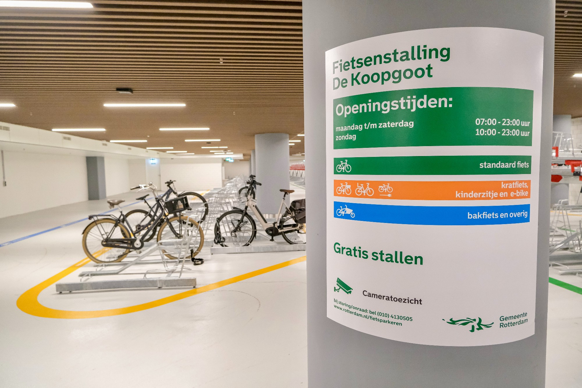 An underground bike parking facility in the city center of Rotterdam contains two-tiered metal racks, decorative lighting fixtures, and wood panelling on the ceiling.