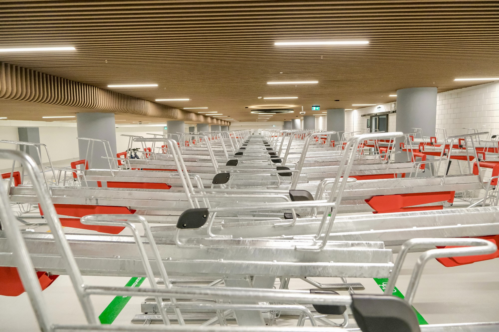 An underground bike parking facility in the city center of Rotterdam contains two-tiered metal racks, decorative lighting fixtures, and wood panelling on the ceiling.