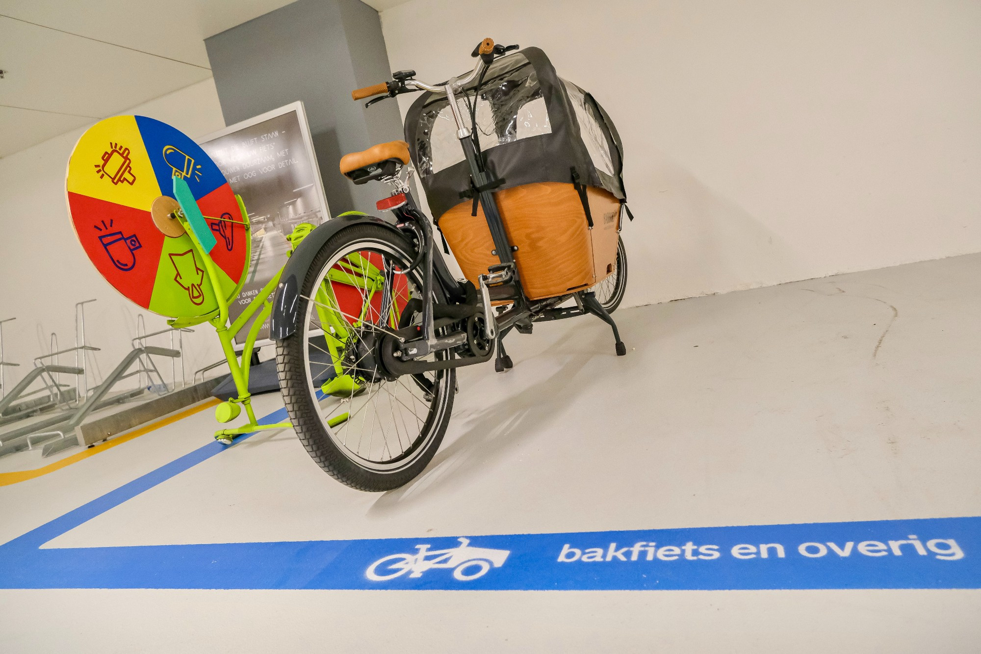 An underground bike parking facility in the city center of Rotterdam contains two-tiered metal racks, decorative lighting fixtures, and wood panelling on the ceiling.