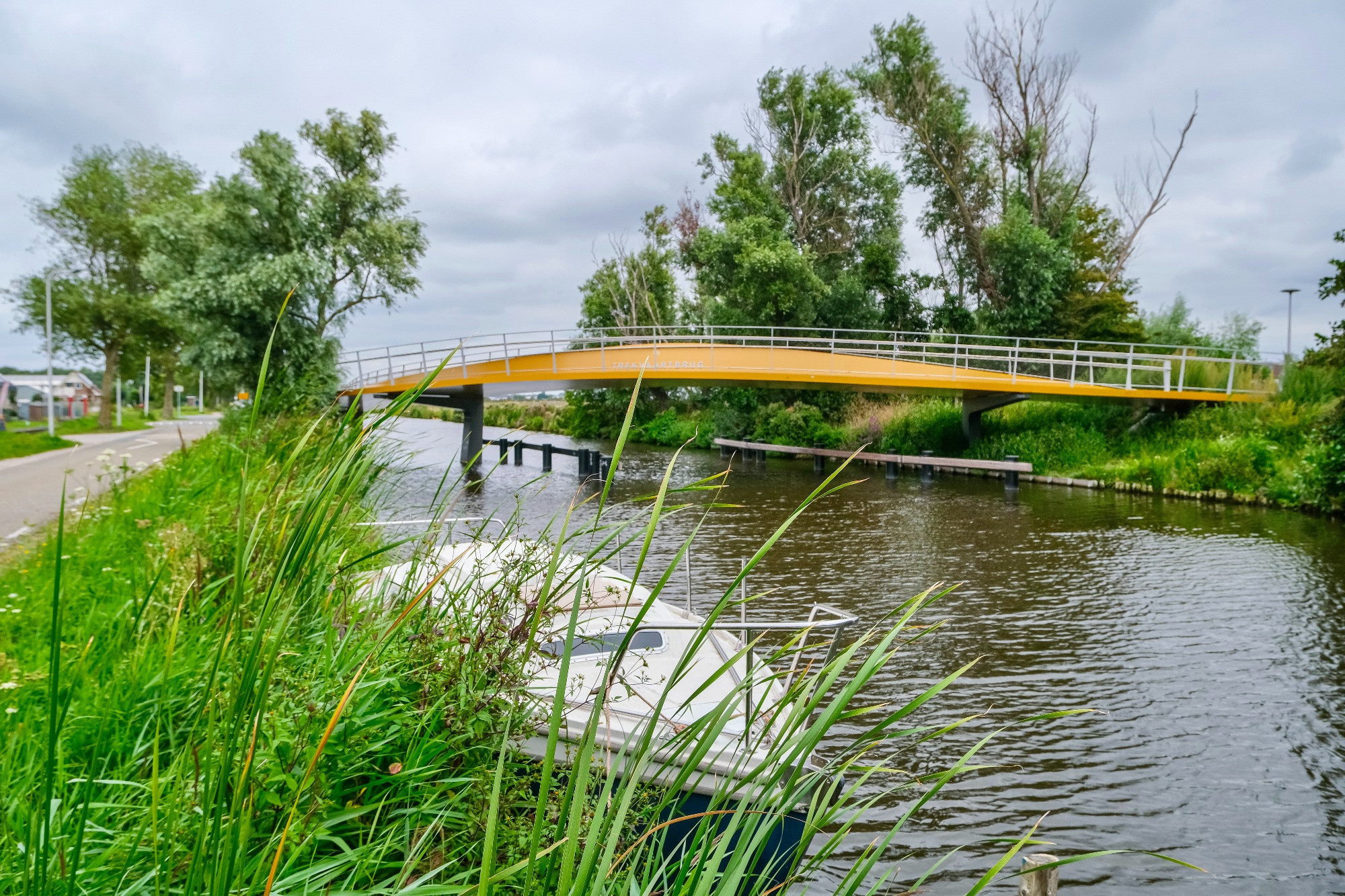 Photographs of a yellow and grey curved steel cycling bridge that stretches across a canal in Voorhout in the rural Netherlands.
