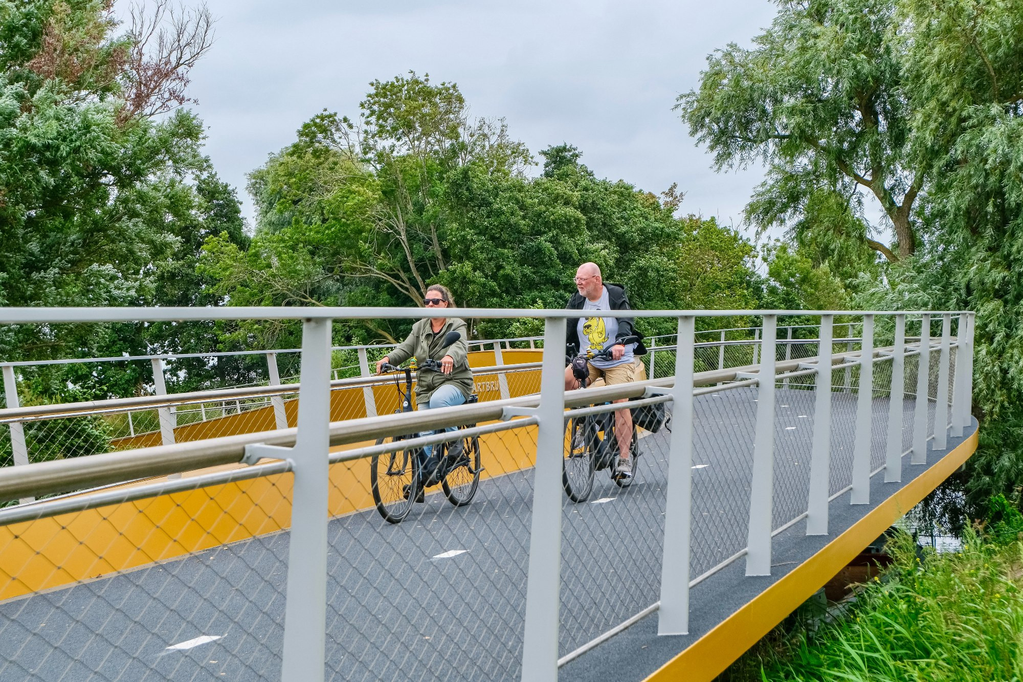 Photographs of a yellow and grey curved steel cycling bridge that stretches across a canal in Voorhout in the rural Netherlands.