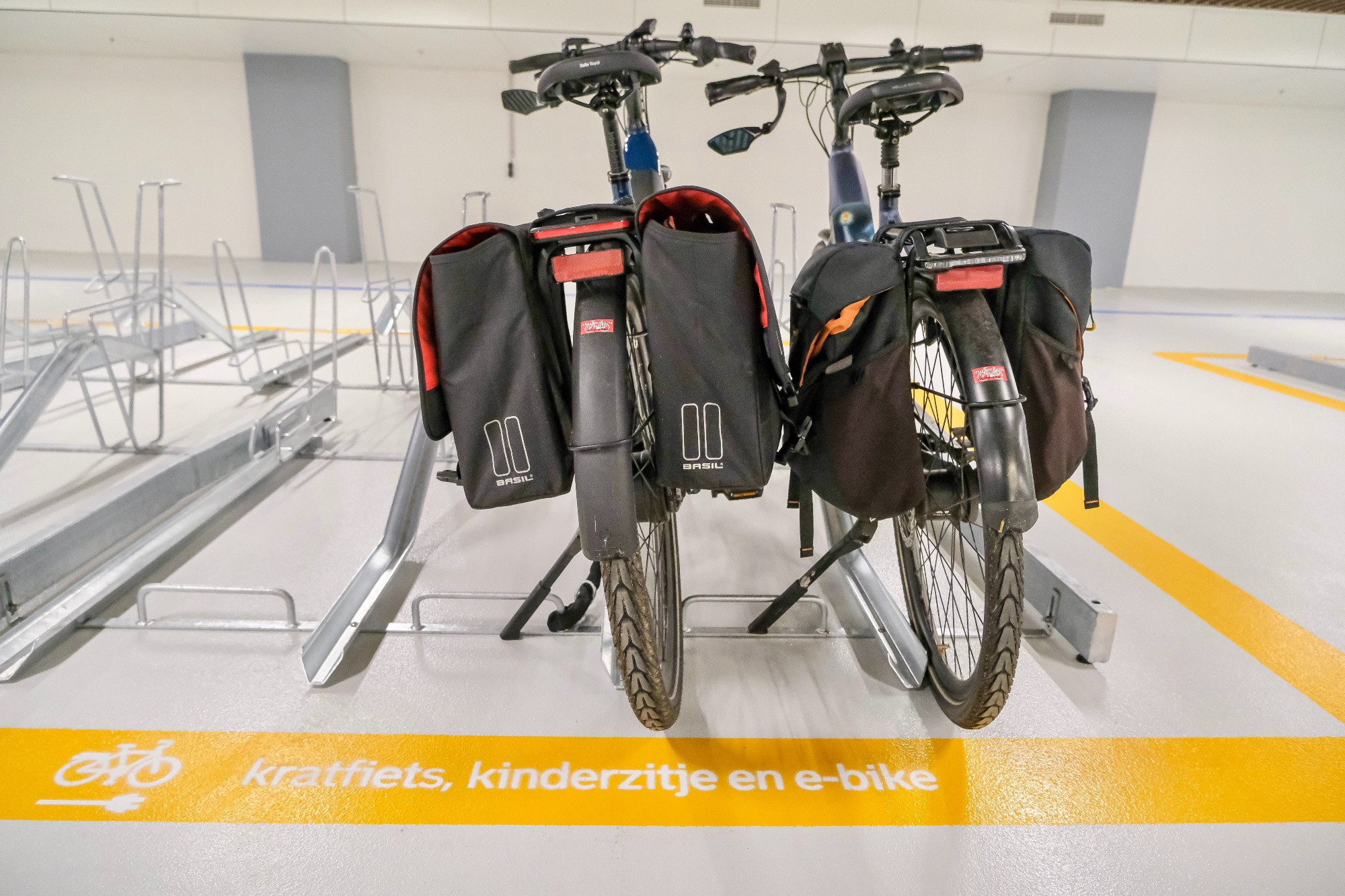 An underground bike parking facility in the city center of Rotterdam contains two-tiered metal racks, decorative lighting fixtures, and wood panelling on the ceiling.