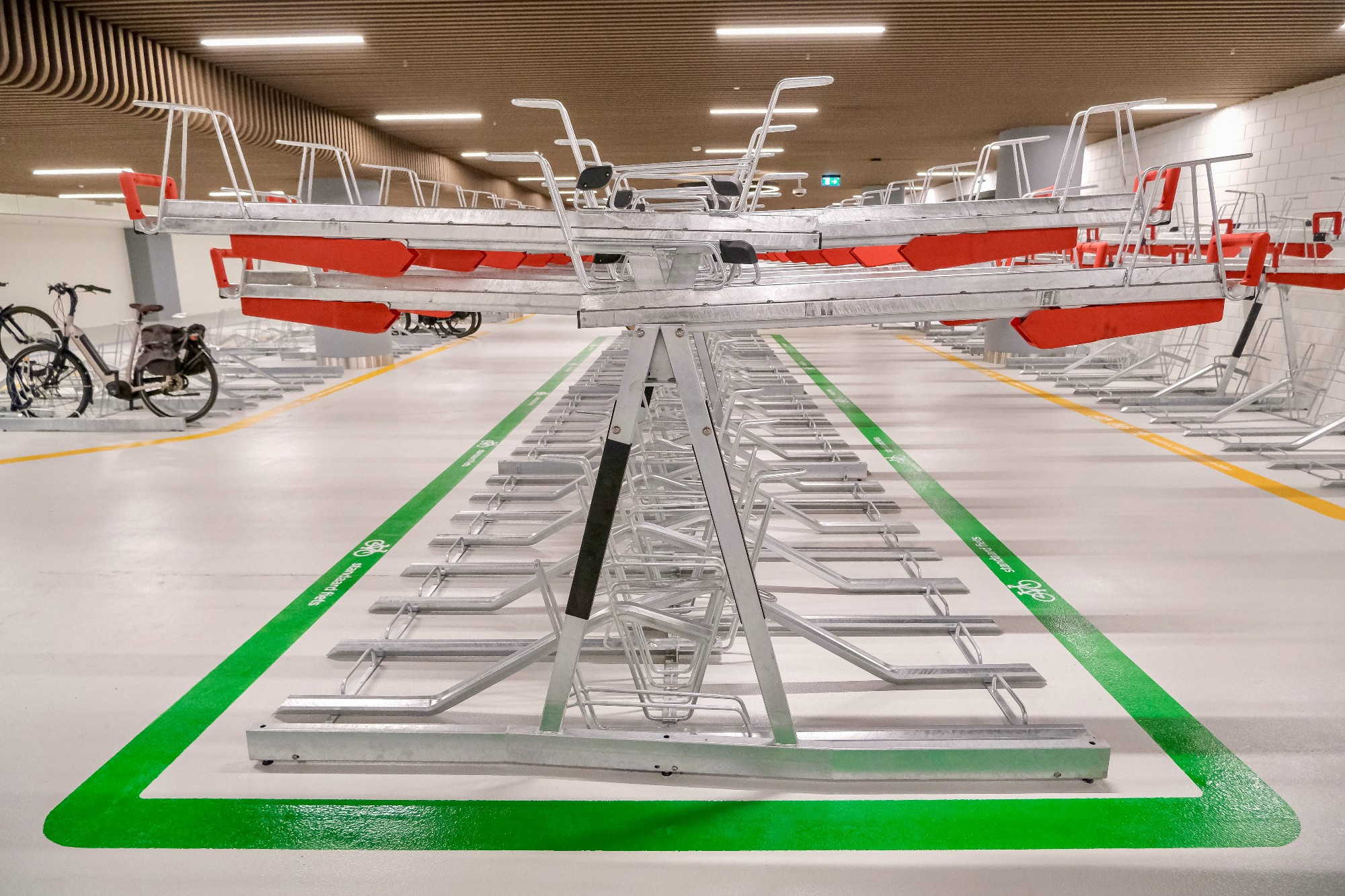 An underground bike parking facility in the city center of Rotterdam contains two-tiered metal racks, decorative lighting fixtures, and wood panelling on the ceiling.