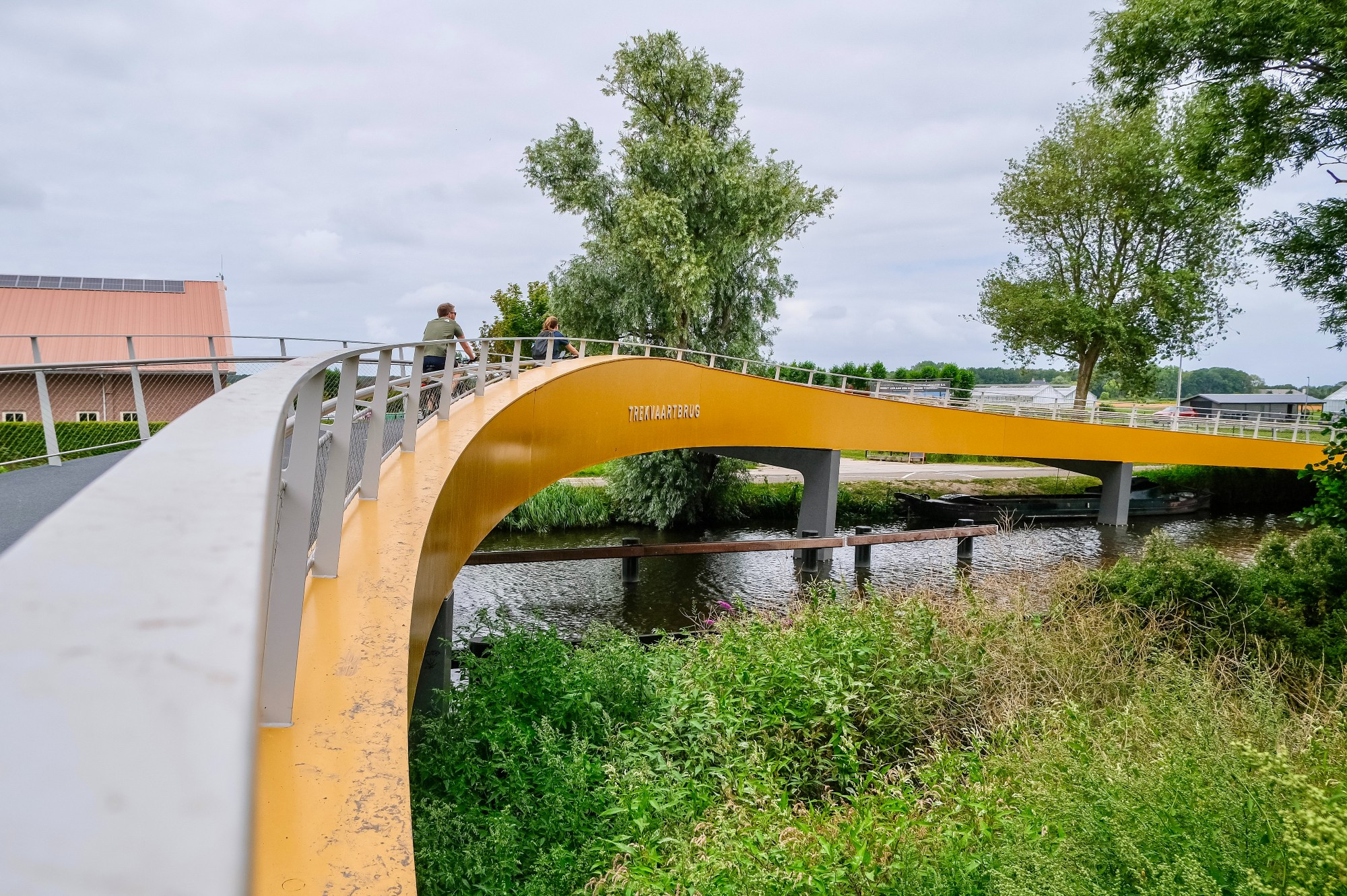 Photographs of a yellow and grey curved steel cycling bridge that stretches across a canal in Voorhout in the rural Netherlands.
