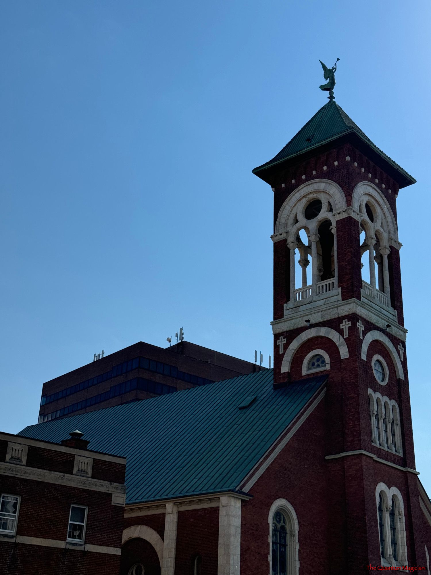 A church steeple above a church roof, the top of an office building slightly visible behind it, and another to the left beside it.