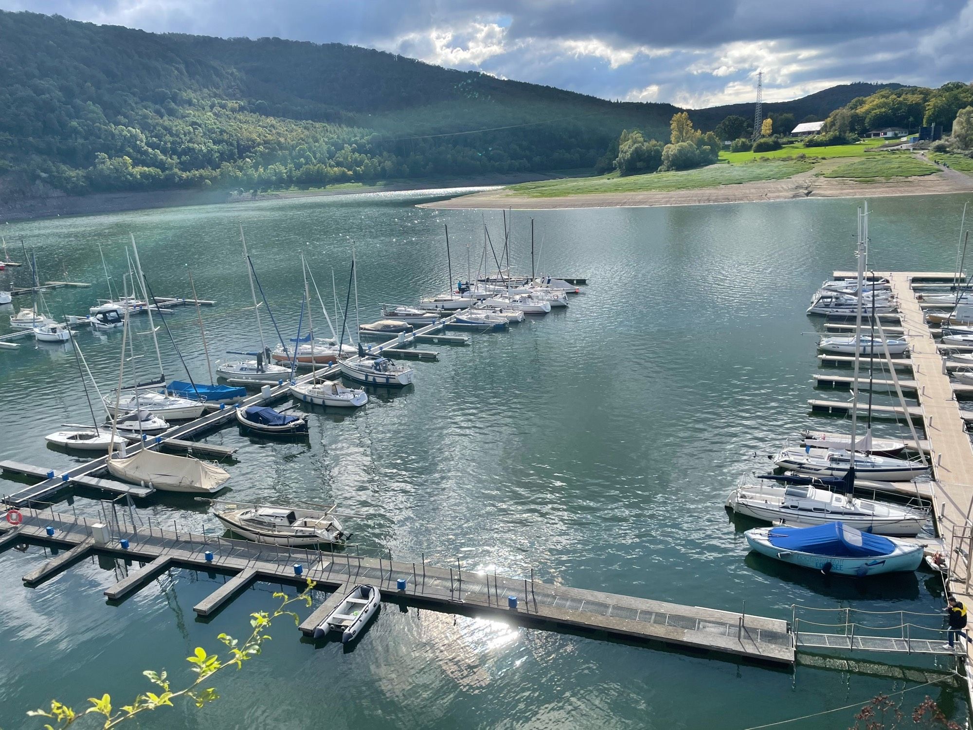 Segelboothafen am See vor bewaldeten Hügeln.