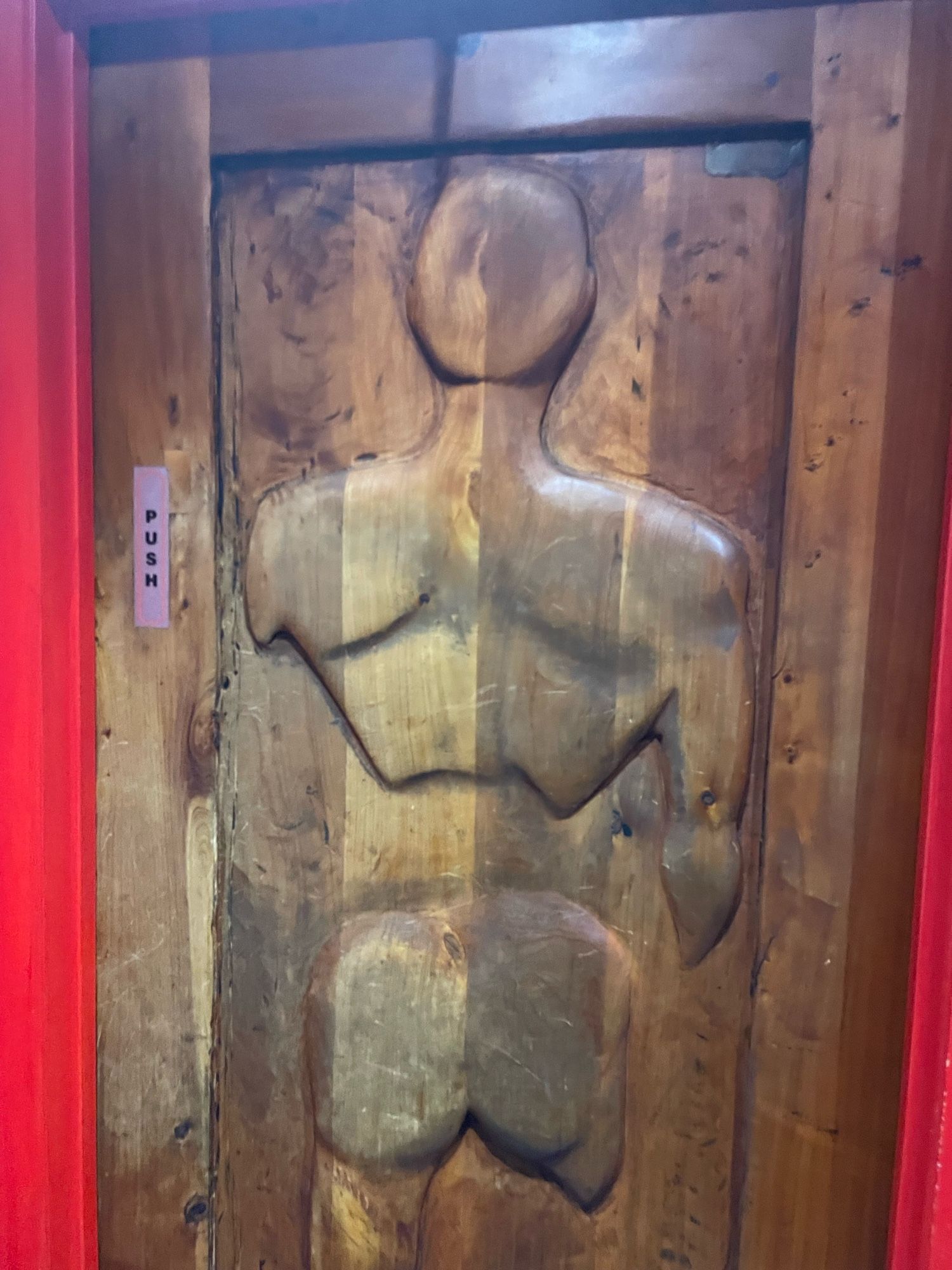 Door to the male bathroom with a carved silhouette of a naked male as seen from behind.