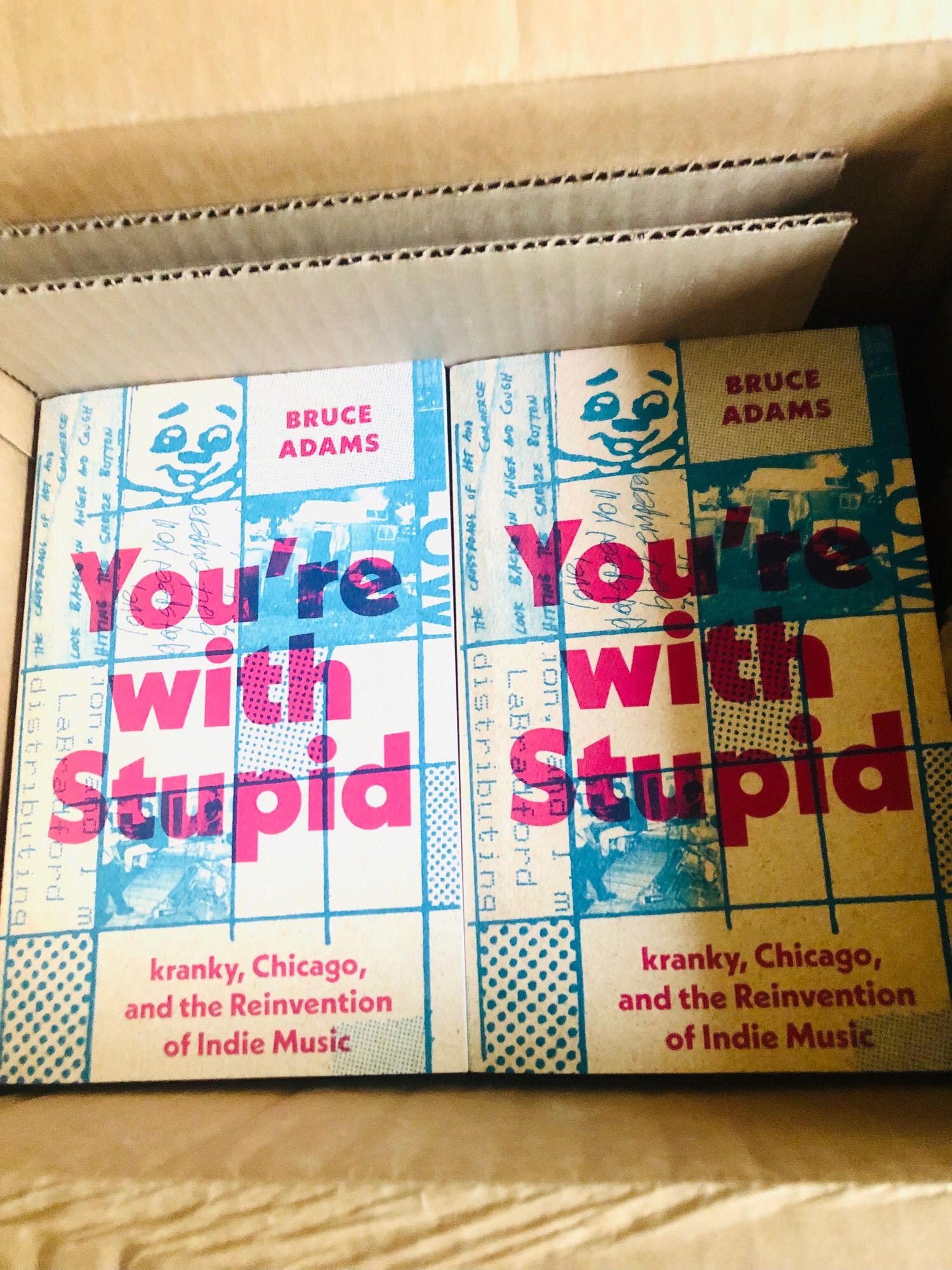 Copies of the paperback edition of “You’re with Stupid” in a cardboard box.