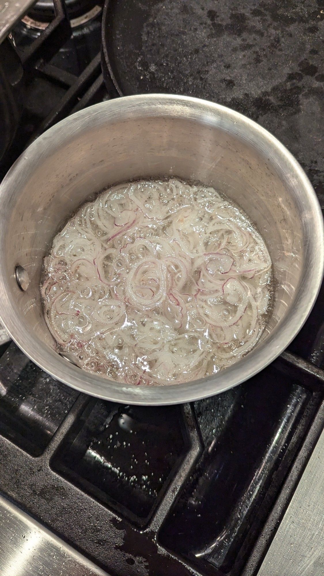 Thinly sliced shallots bubbling in a pot of oil