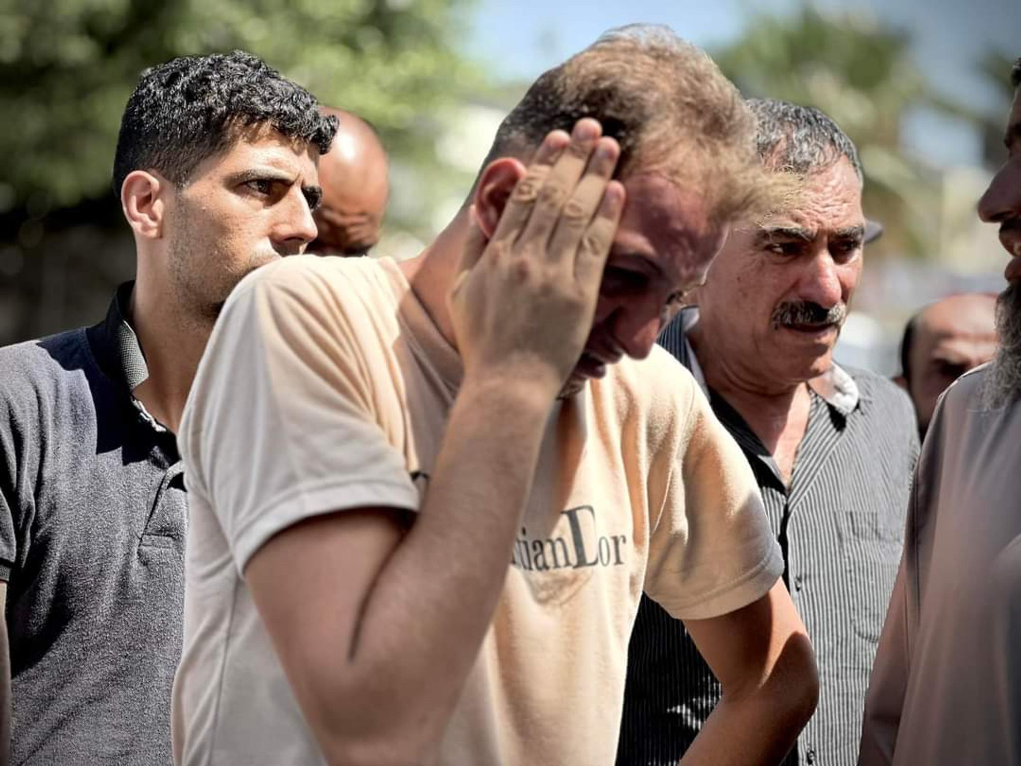 Mohammad Abu al-Qumsan stands outside the hospital, weeping with his hand at his temple, with other men around him as they finish prayers over the bodies of his twins, wife and mother-in-law.