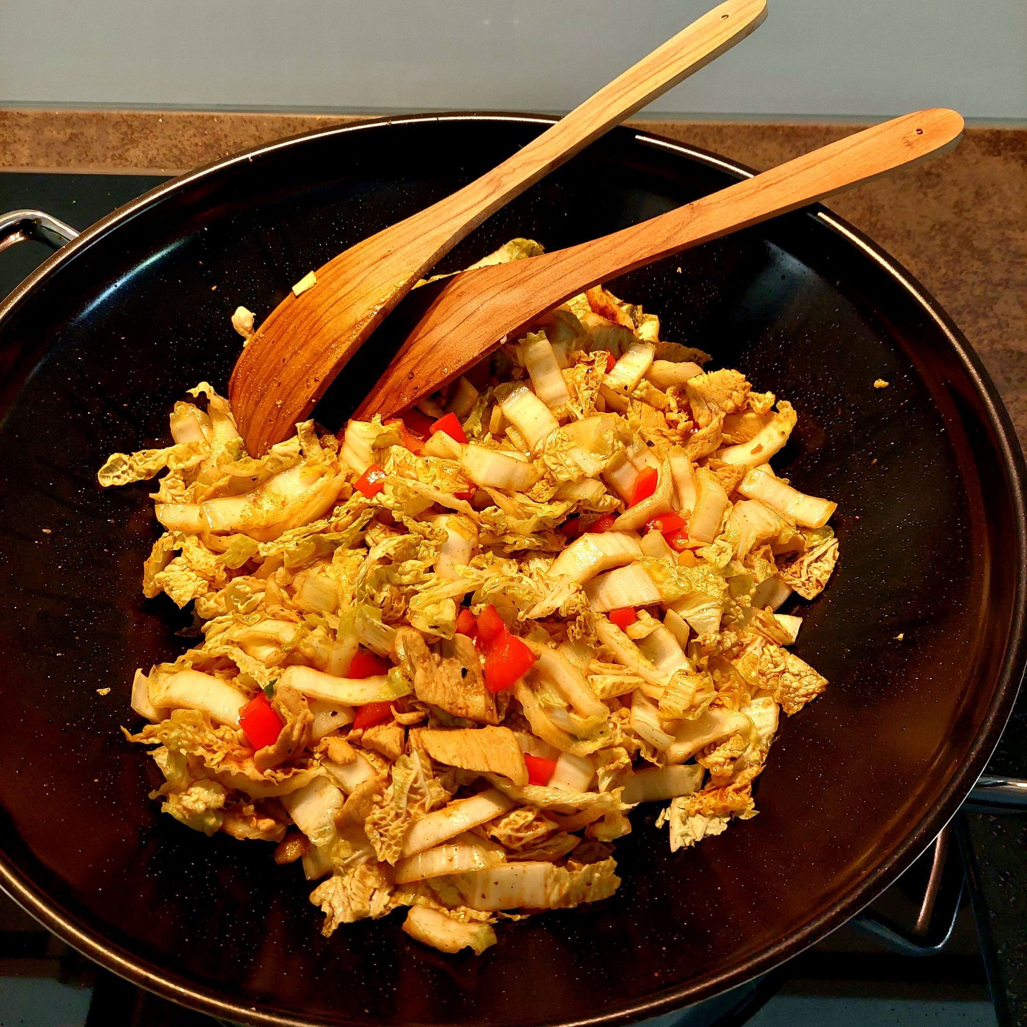 Schwarze Wokpfanne gefüllt mit Chinakohl, rotem Peperoni (Paprika) und Pouletgeschnetzeltem. Gewürzt mit u.a. Kurkuma, Koriandersamen und Pfeffer.