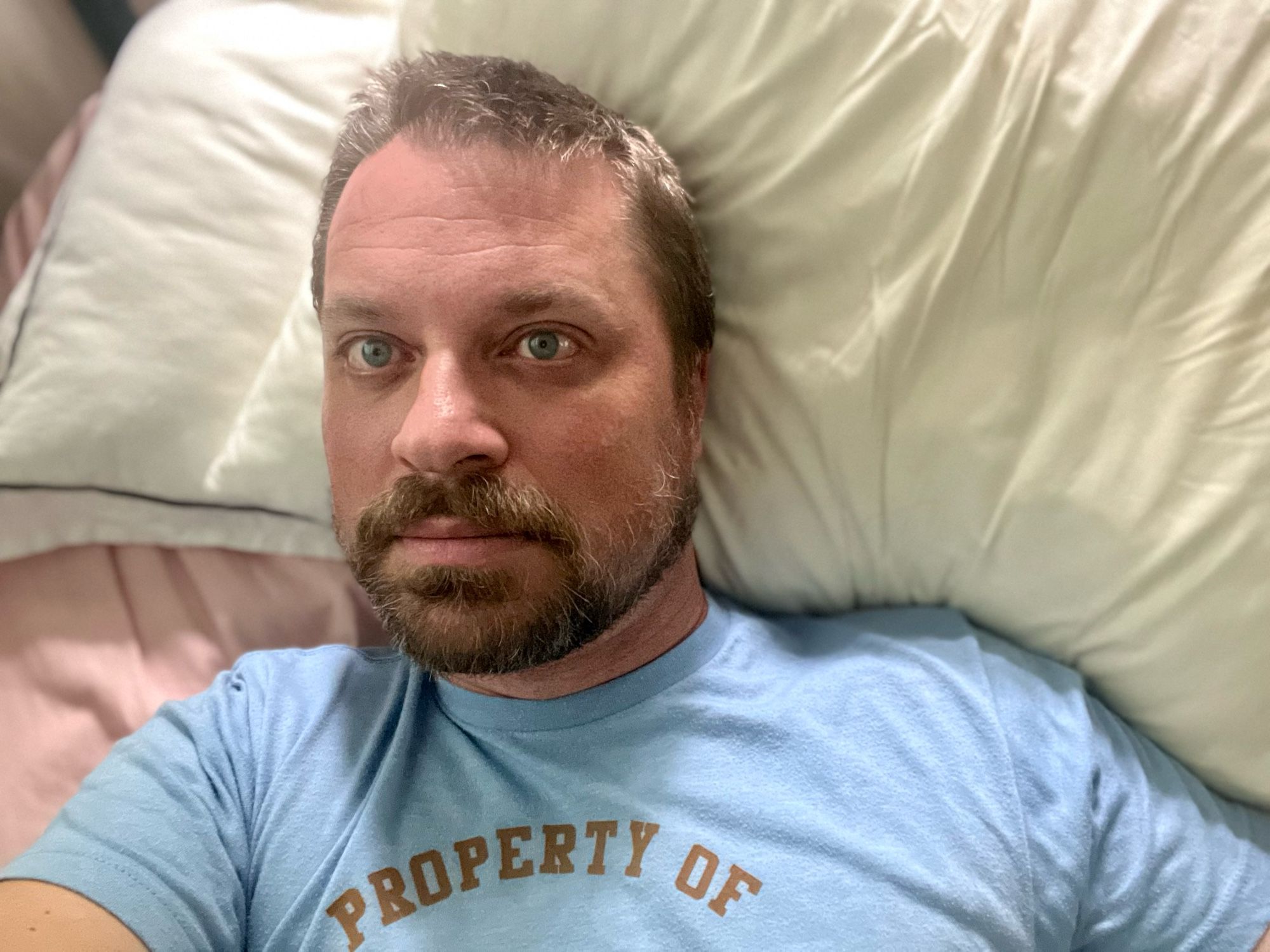 I’m lying on pink sheets and a white pillow. My shirt is the color of my eyes and you can see the top of it, which says, “property of.” It’s a Sudbury Bulldogs shirt from Shoresy.