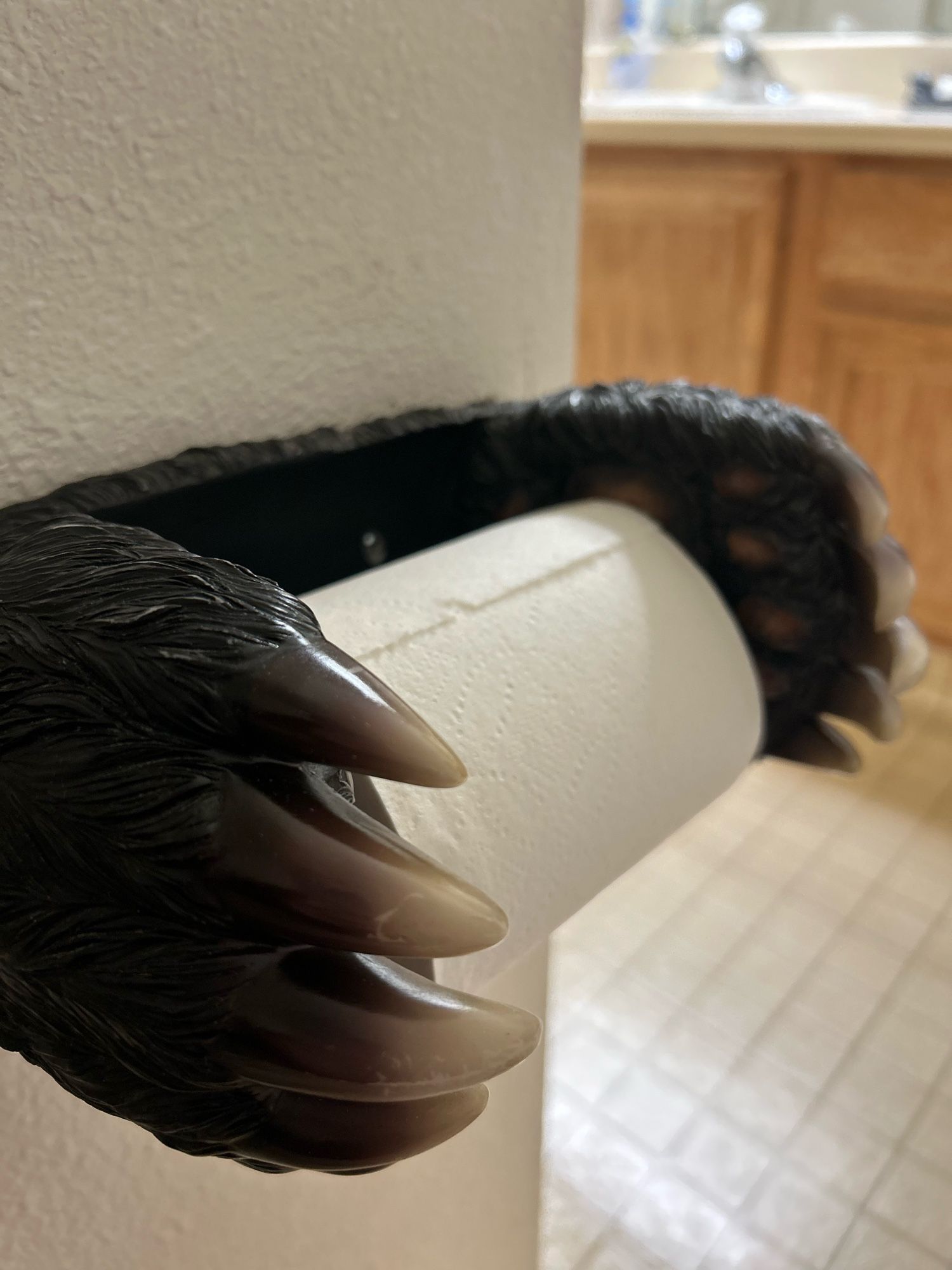 A toilet paper holder that has two plastic bear paws holding the roll in place.