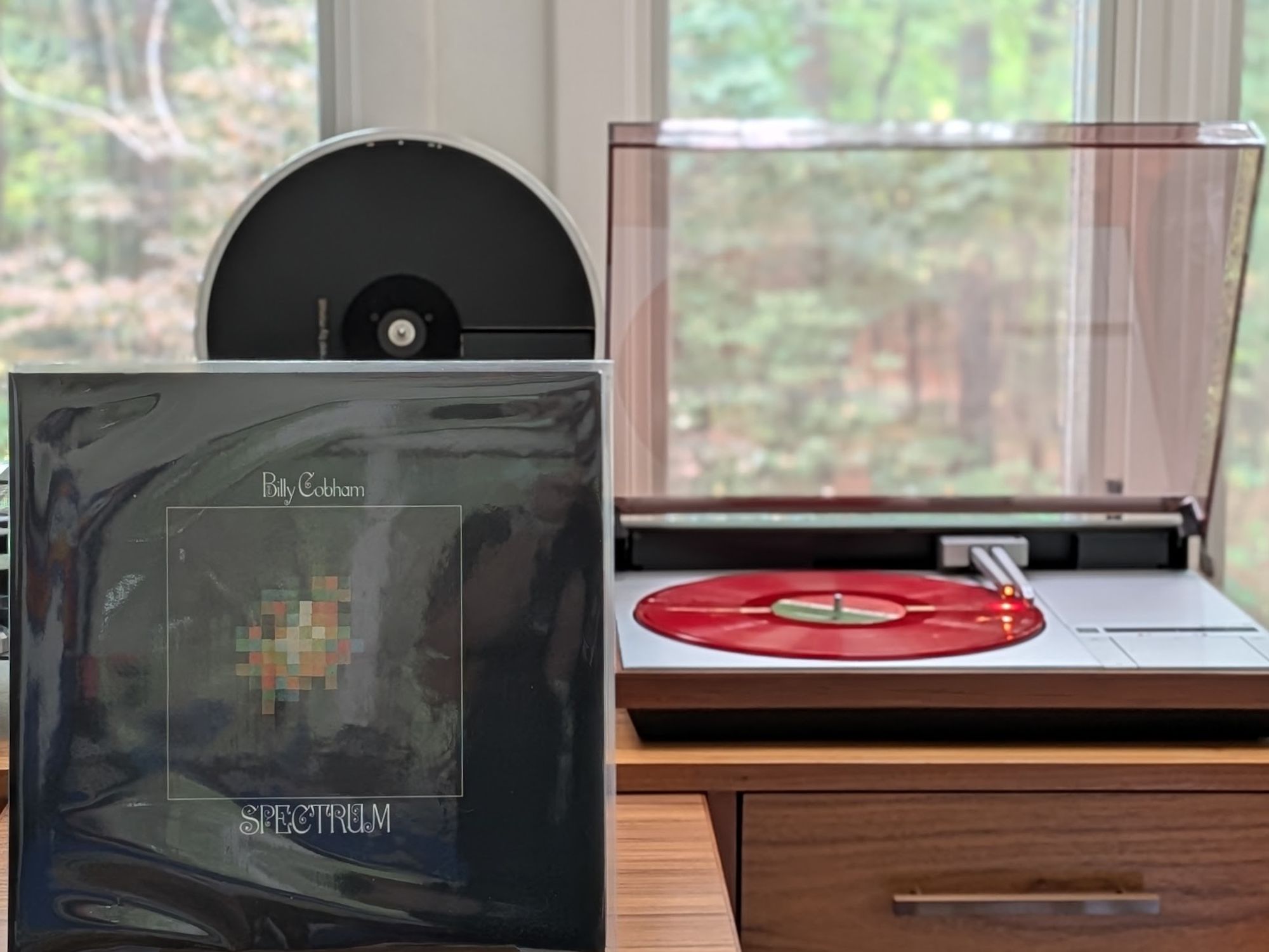 Billy Cobham - Spectrum LP cover.

A kind of space starburst, very low-res, on a black background, with a thin white frame. There are a lot of reflections. Sorry,

The red LP plays on a vintage, restored Bang & Olufsen Beogram 4000 linear-tracking turntable to the right.