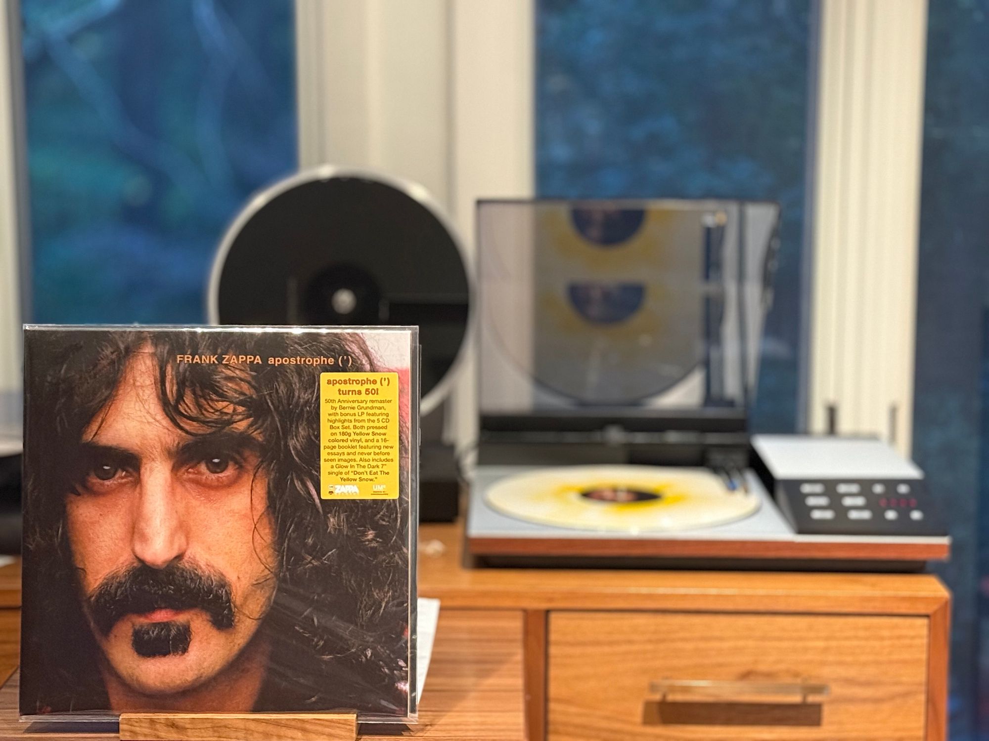 Frank Zappa - apostrophe (‘) LP cover.

A close-up portrait of Frank Zappa’s face, trademark mustache, mop of hair, looking directly into the camera.

The yellow-streaked white LP plays on a vintage, restored Bang & Olufsen Beogram 8002 linear-tracking turntable to the right.