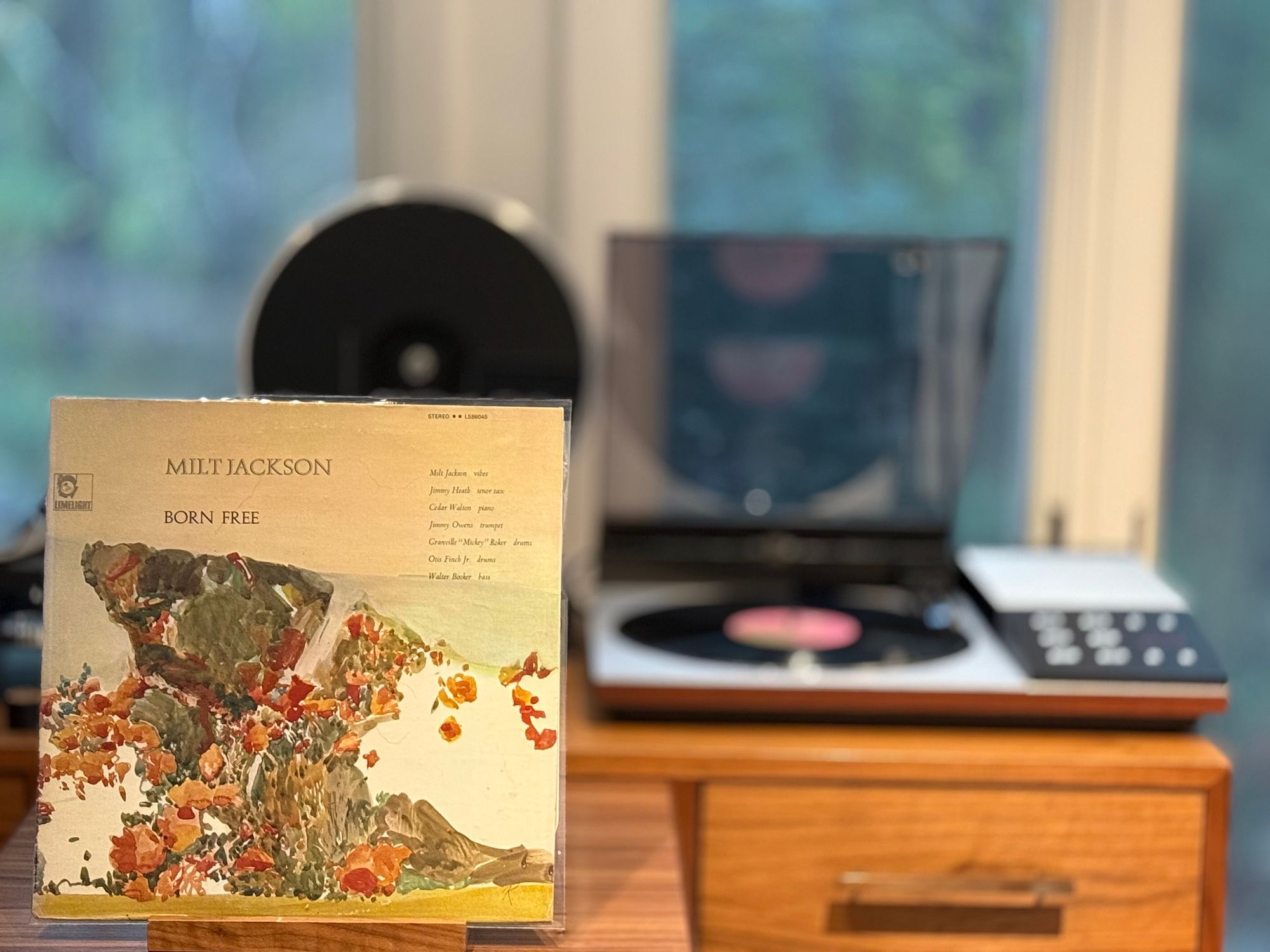 Milt Jackson - Born Free LP cover.

A watercolor landscape, with a large rock to the upper left and flowers and sand/dirt below. Title above left with players above right.

The black LP plays on a vintage, restored Bang & Olufsen Beogram 80002 linear-tracking turntable to the right.