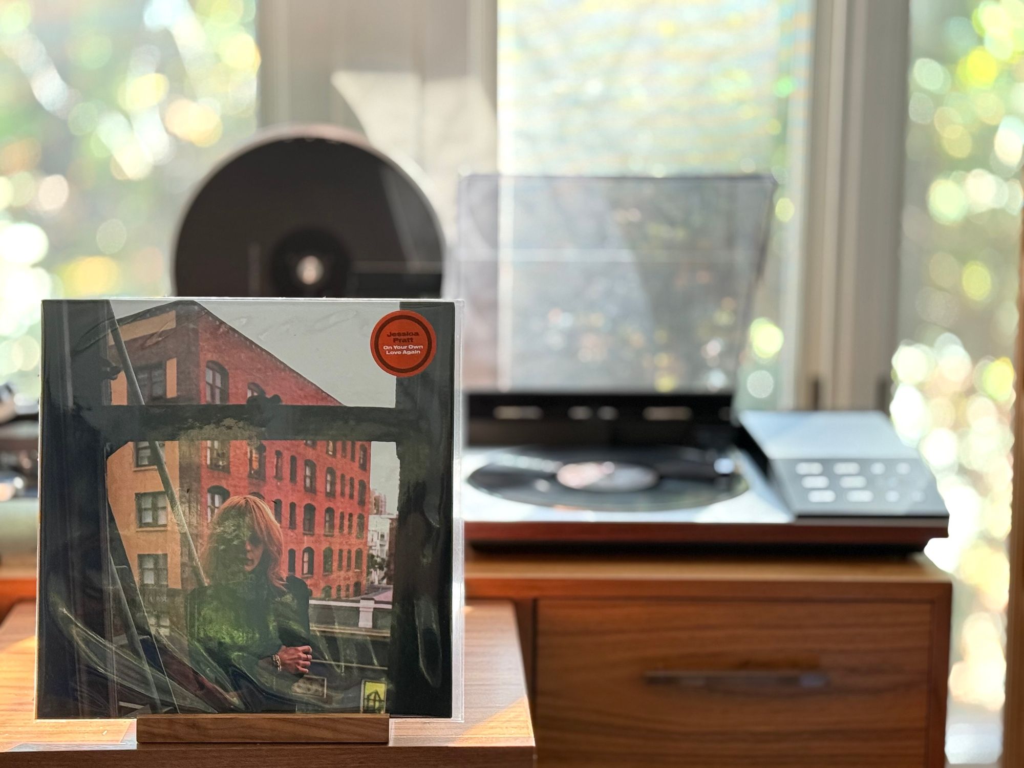 Jessica Pratt - On Your Own Love Again LP cover.

Jessica Pratt, blond hair, dark jacket, arms crossed, in front of a window, with an apartment building visible outside.

The black LP plays on a vintage, restored Bang & Olufsen Beogram 8002 linear-tracking turntable to the right.