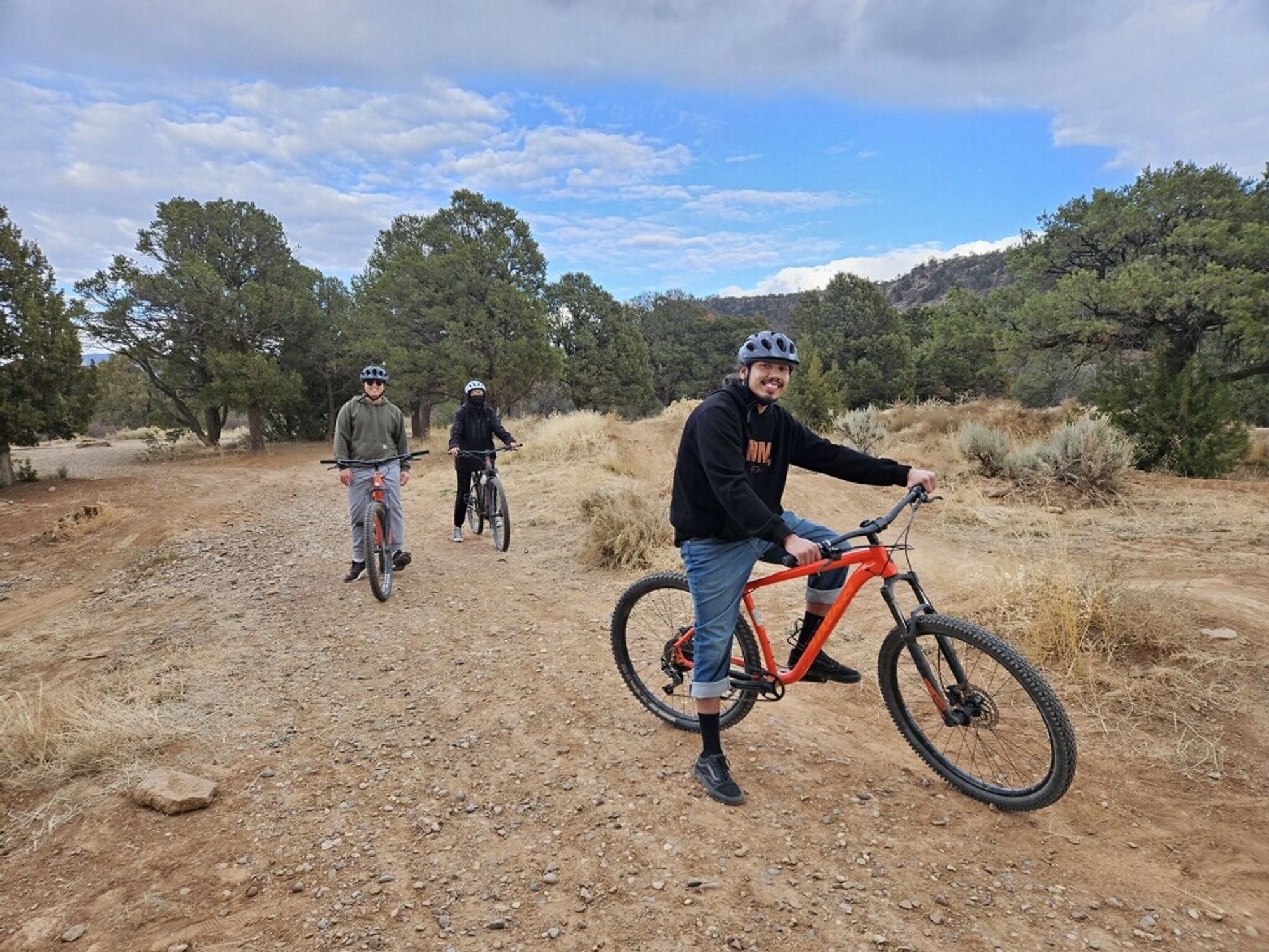 Three people on mountain bikes on a trail with trees in the background.